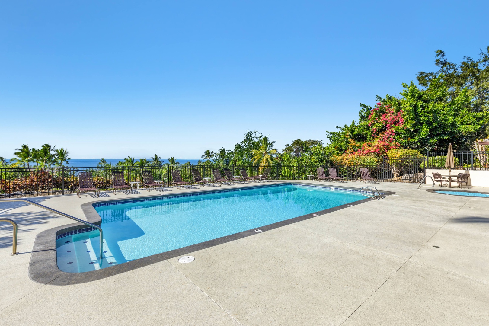 A sparkling outdoor pool overlooking tropical palms and the sea, with ample lounge chairs and lush gardens framing the sunny deck.