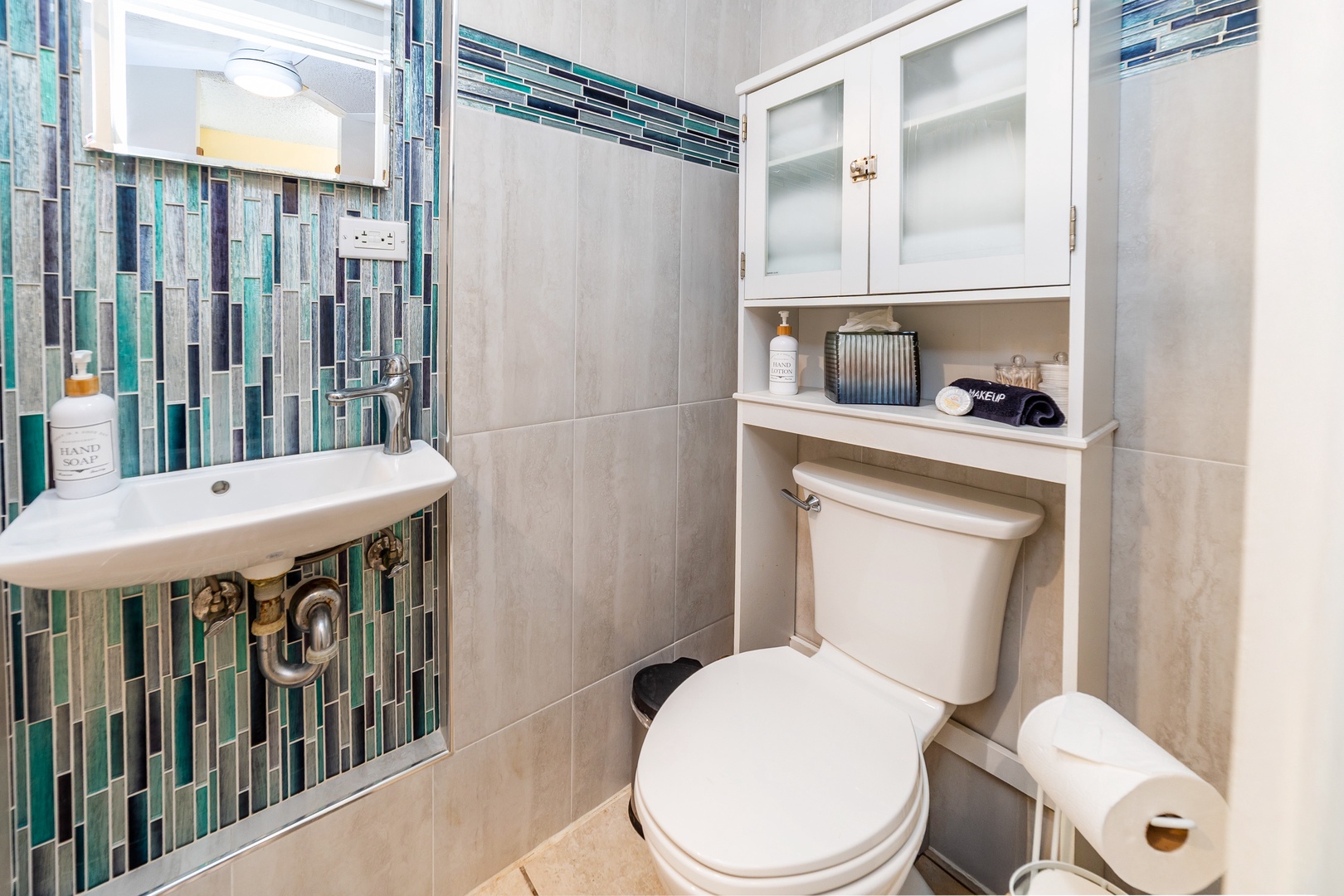 Step into your private bathroom featuring stunning ocean-inspired glass tile work, a space-saving pedestal sink, and thoughtful storage solutions that blend coastal charm with modern comfort.