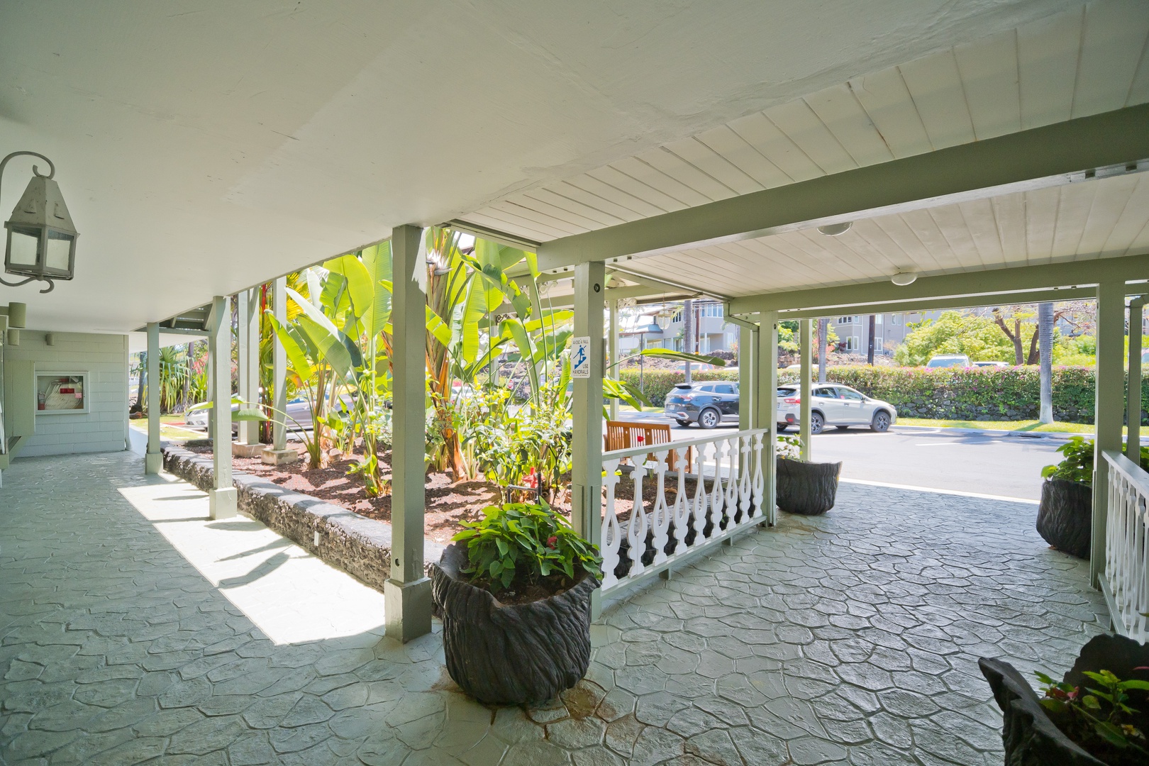 A covered entrance with white columns and lush tropical greenery welcomes arrivals, featuring decorative railings and patterned stone flooring that frames views of the surrounding neighborhood.