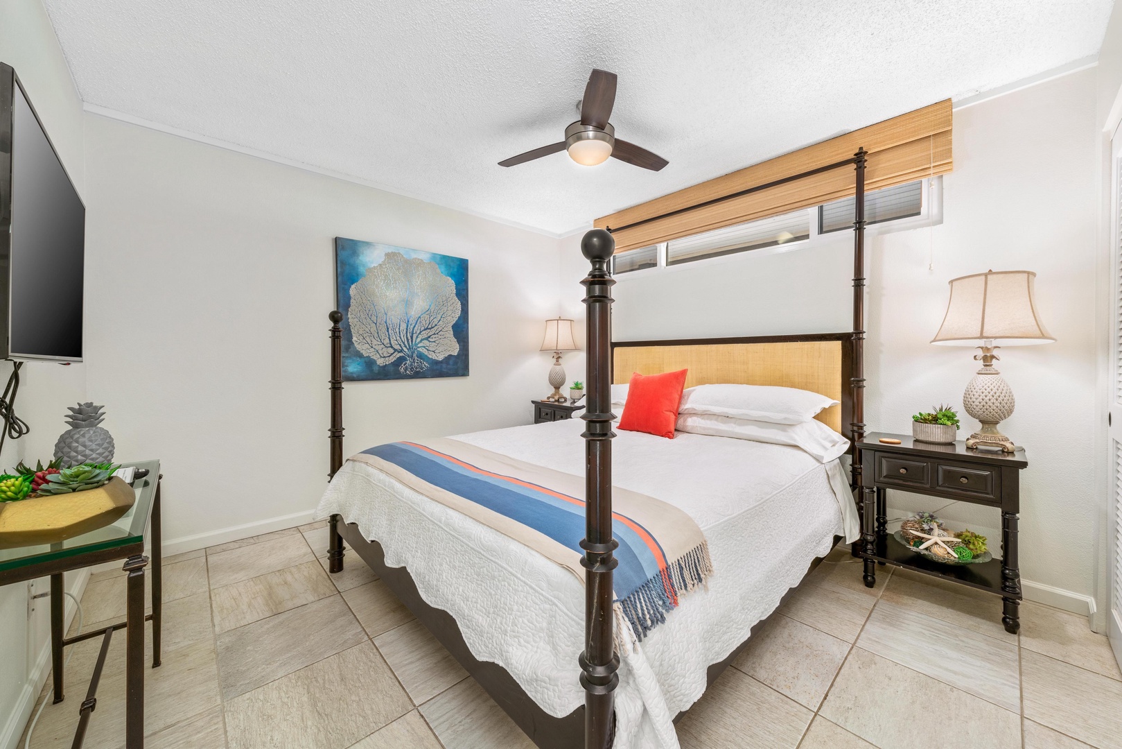 Drift off beneath a coastal four-poster bed in your serene retreat, where soft linens and gentle breezes from the ceiling fan promise restful nights.