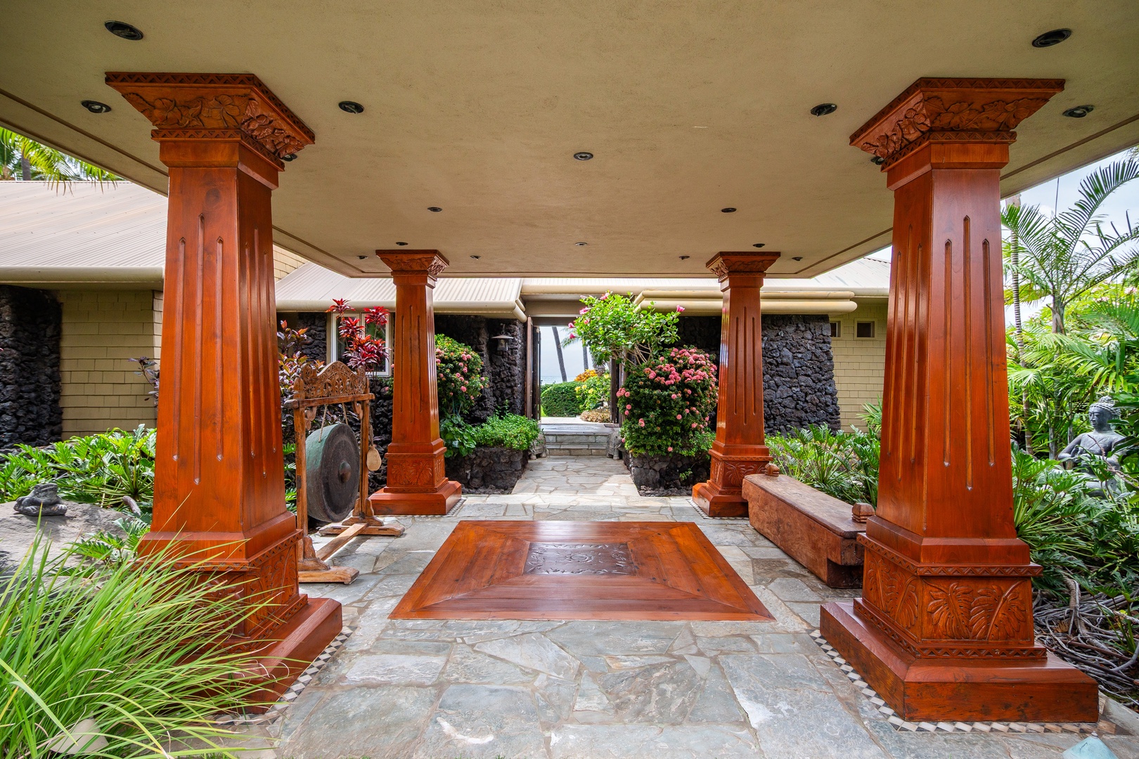 The property's entrance features ornate carved columns and tropical landscaping, creating an elegant arrival experience framed by lush greenery and traditional architectural details.