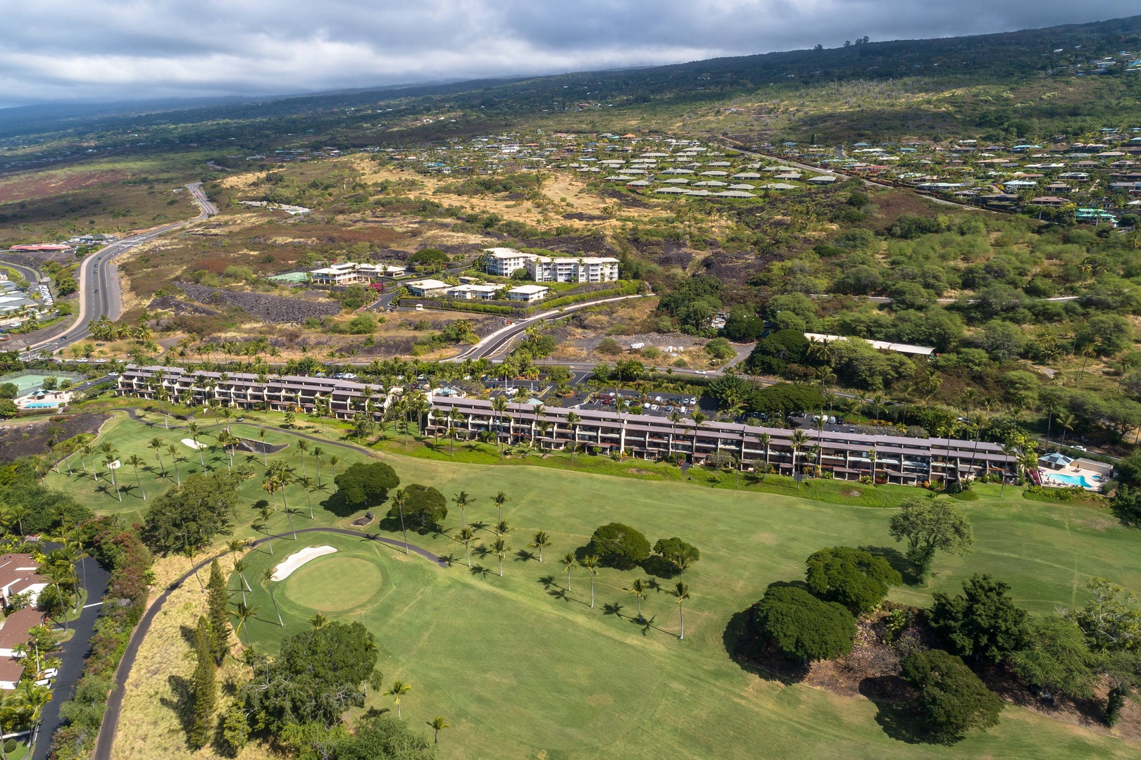 Aerial view of the vacation rental property set within a lush golf course surrounded by rolling hills, natural landscape, and residential neighborhoods, offering a scenic island setting.