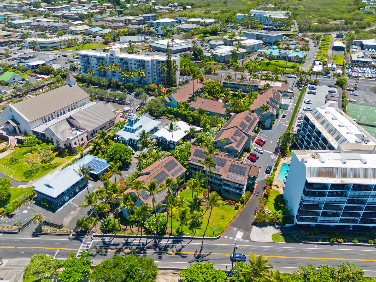 Aerial view of a tropical resort community featuring lush landscaping, palm trees, and residential buildings near shopping areas and recreational facilities.