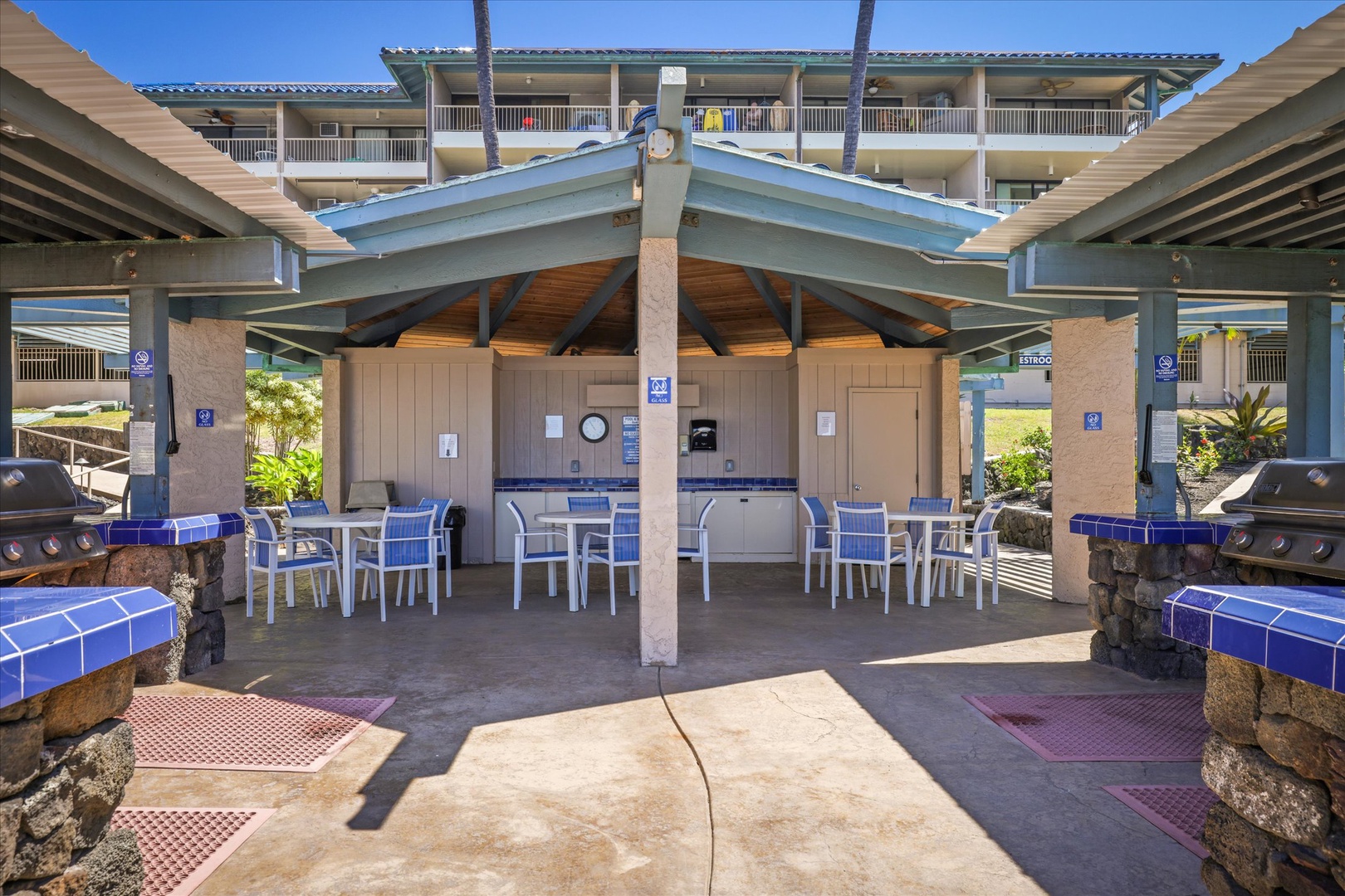 The communal outdoor kitchen and dining pavilion features built-in grills, tiled prep counters, and shaded seating—a welcoming space for guests to gather, cook, and share meals together in the Hawaiian sunshine.