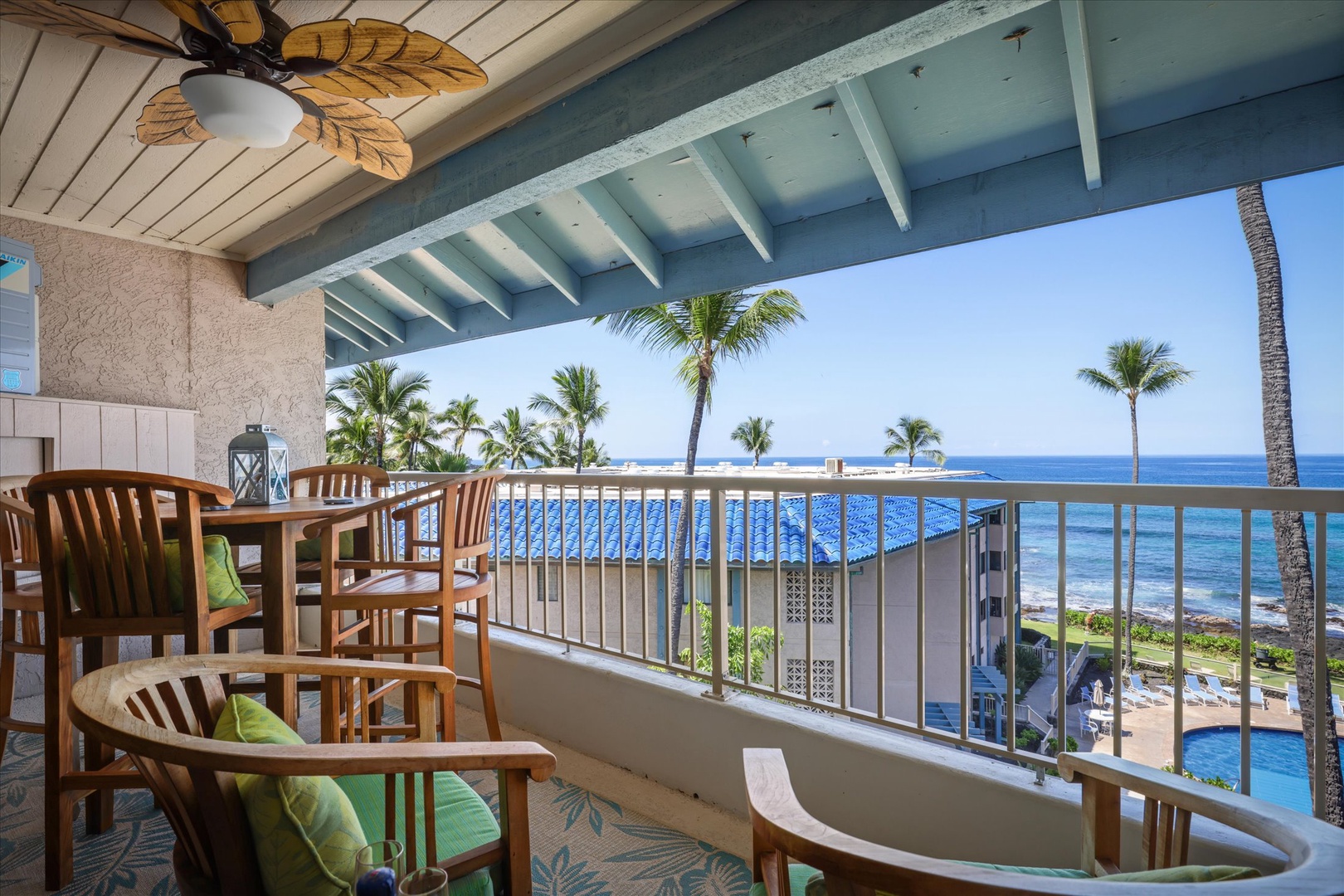 Spacious oceanfront lanai with comfortable seating, tropical ceiling fan, and stunning views of swaying palms, azure waters, and the sparkling pool below.