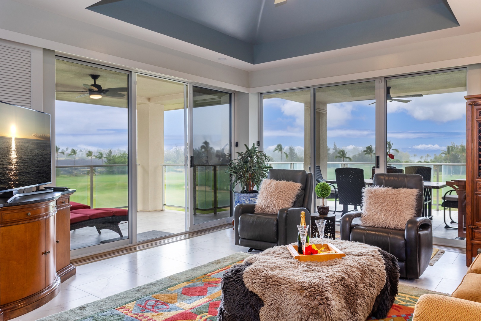 Relax in your spacious living room with plush seating and floor-to-ceiling glass doors opening to your private balcony overlooking lush greens and tropical palms.