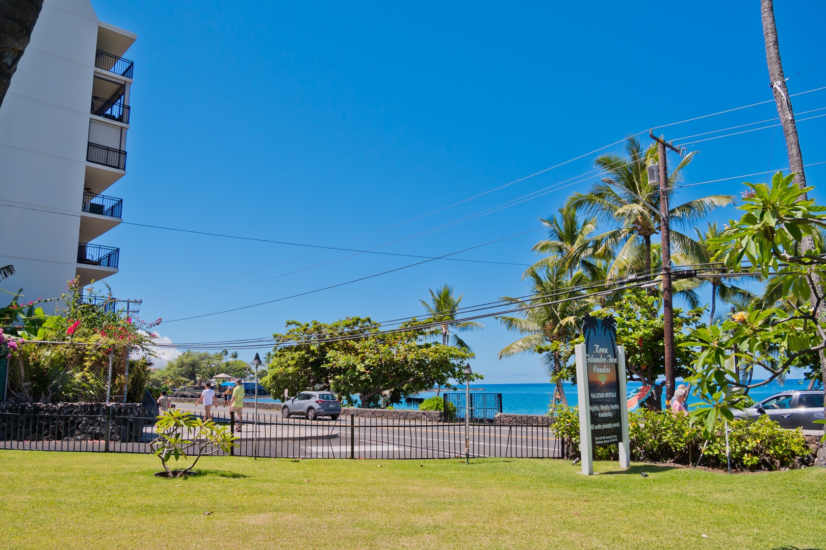 A beachfront property located steps from the turquoise ocean, surrounded by swaying palm trees and tropical gardens under clear blue skies on a beautiful sunny day.