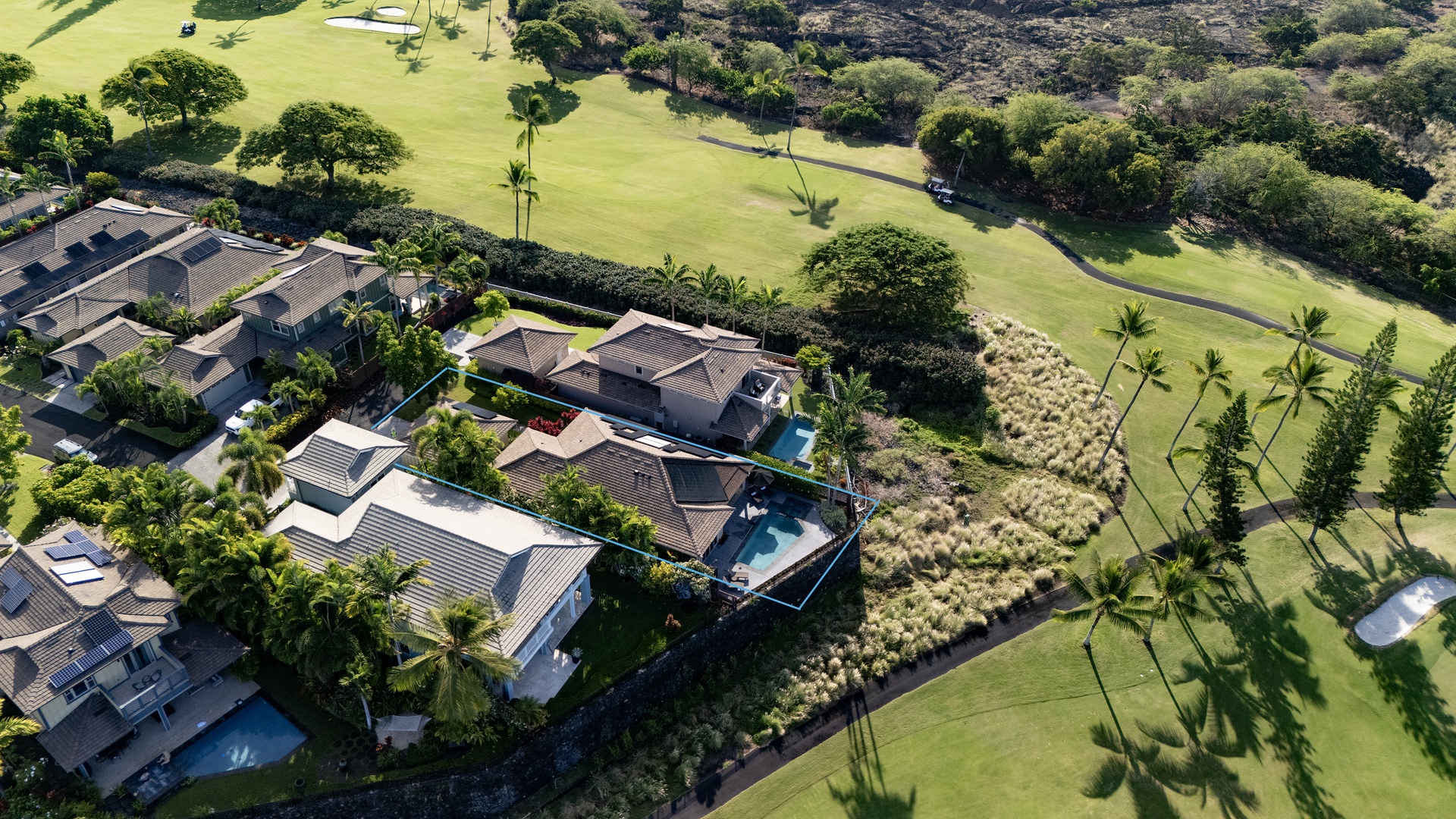 Stunning aerial view of Holua Kai nestled alongside an emerald golf course with swaying palm trees and tropical landscaping.