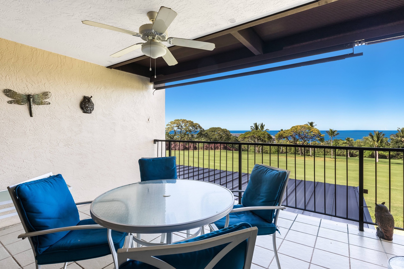 Imagine your morning coffee here—a covered balcony overlooking lush greens and sparkling ocean, with a ceiling fan keeping you cool and comfortable.