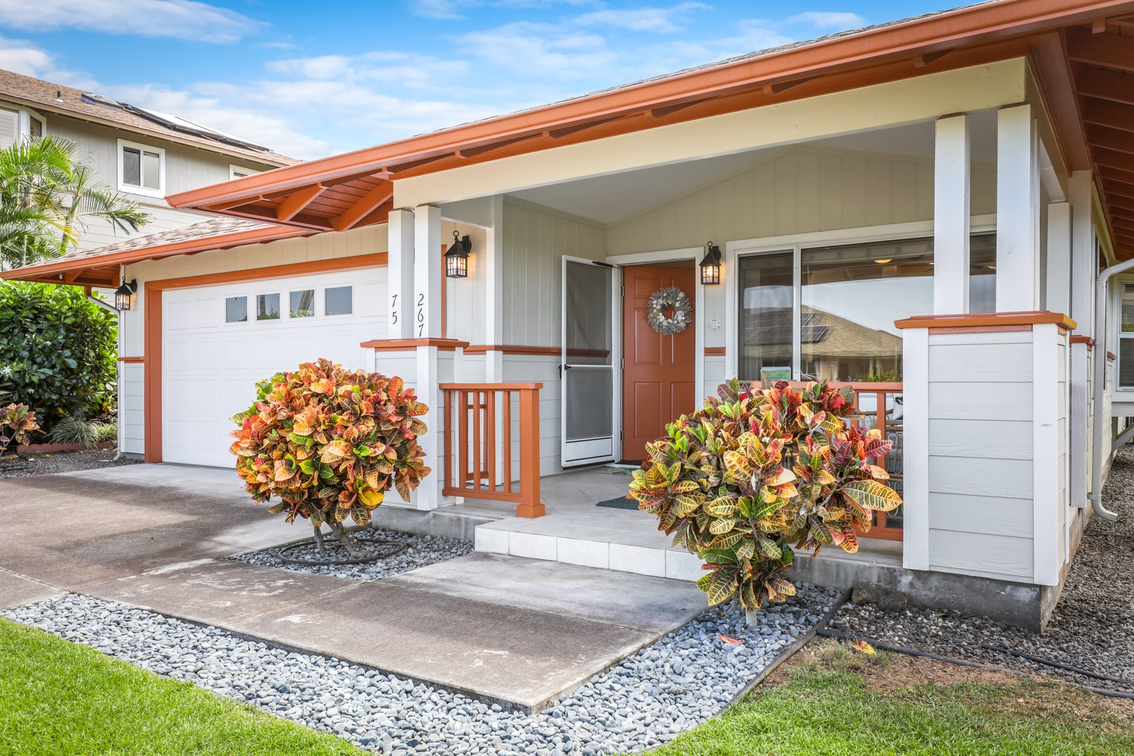 A welcoming single-story home with tropical charm, featuring a covered entryway adorned with vibrant tropical foliage, convenient garage parking, and modern island-style architecture in a peaceful residential setting.