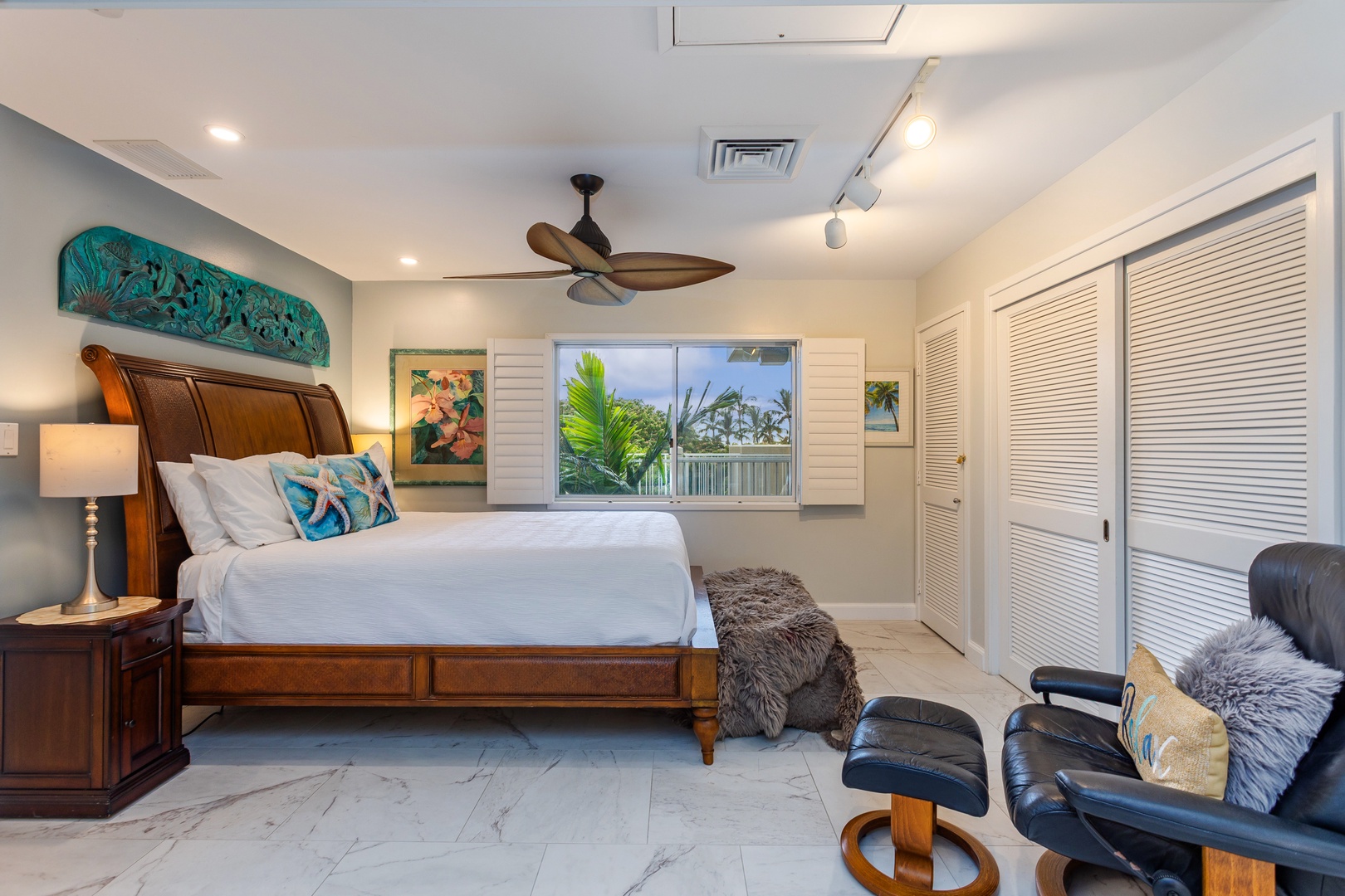 Your bright, airy bedroom retreat features a plush bed dressed in crisp linens, tropical garden views through shuttered windows, and a cozy seating nook for morning coffee or evening relaxation.