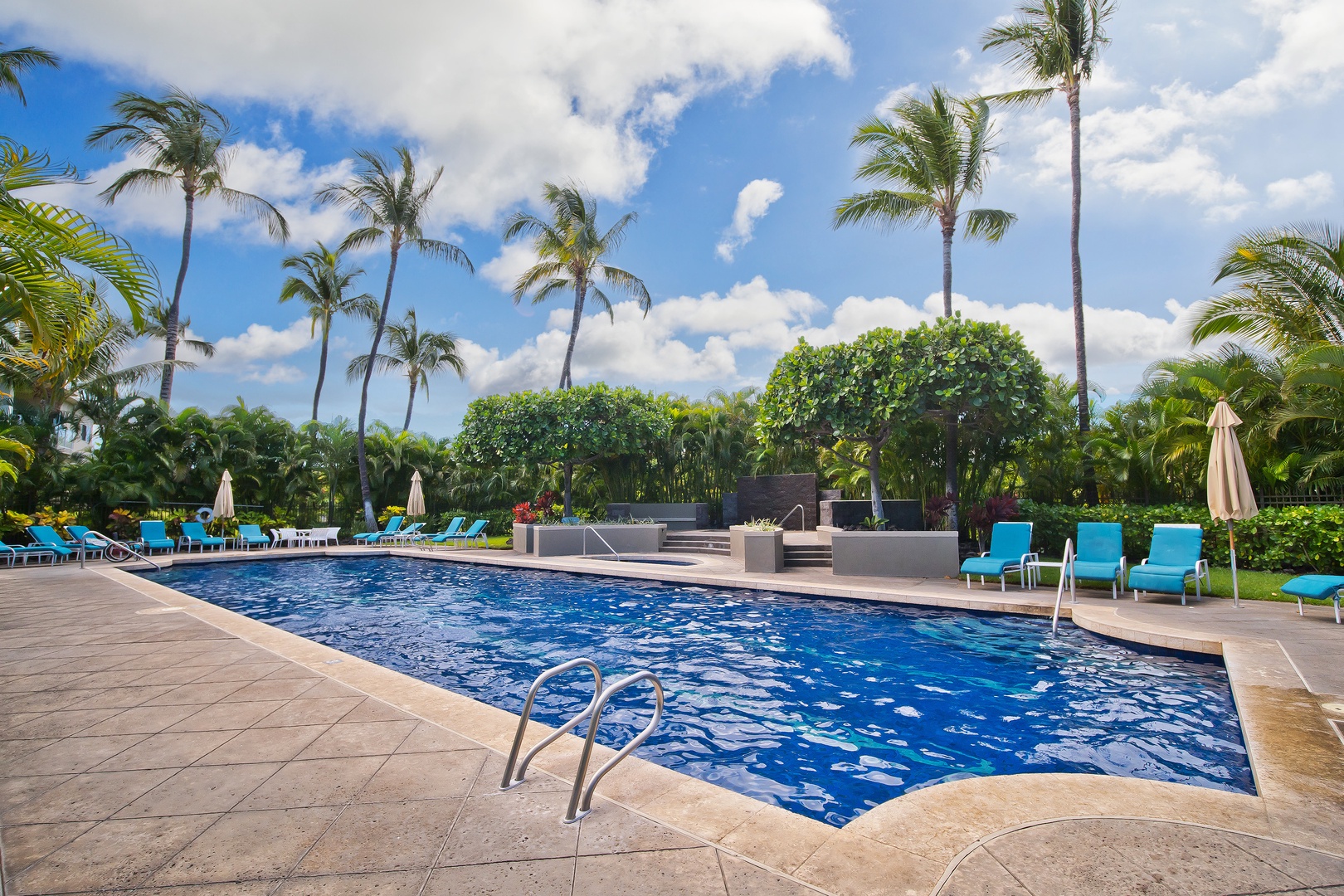 A sparkling pool surrounded by tropical palms and bright blue loungers, perfect for relaxing under sunny skies in your private paradise.