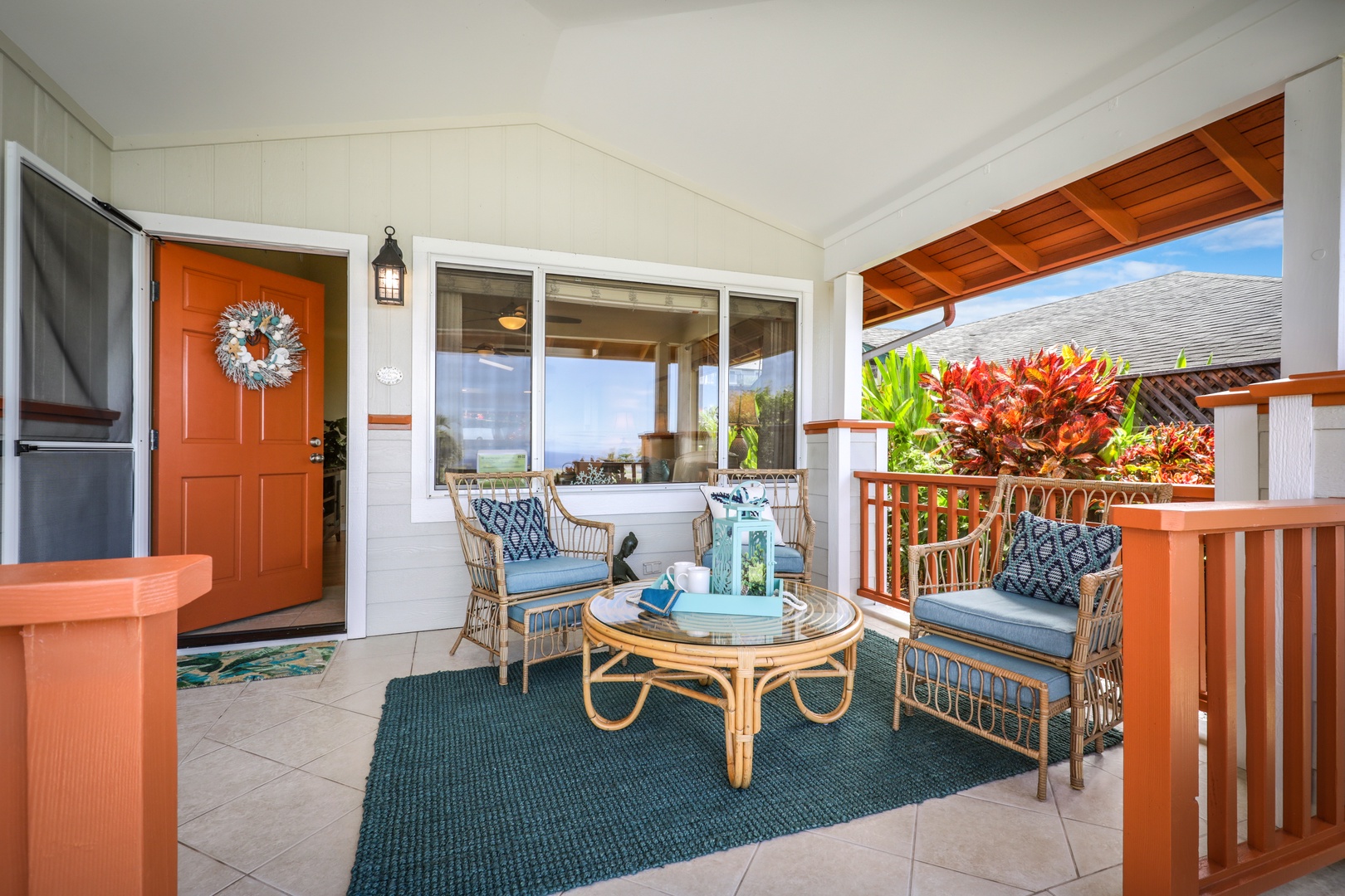 Picture yourself unwinding on this inviting covered lanai, where comfortable rattan seating and vibrant tropical plants create your perfect island retreat with glimpses of blue skies beyond.