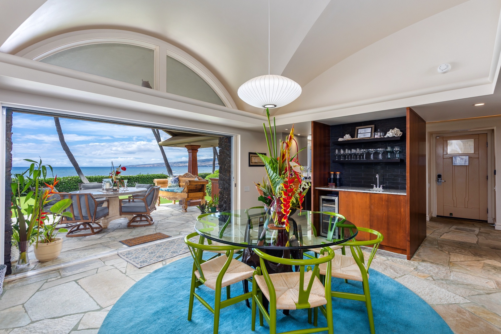 Step into your open-concept dining, where soaring arched ceilings meet ocean breezes. You'll savor meals at the round glass table while gazing at swaying palms and endless blue waters just beyond your terrace.