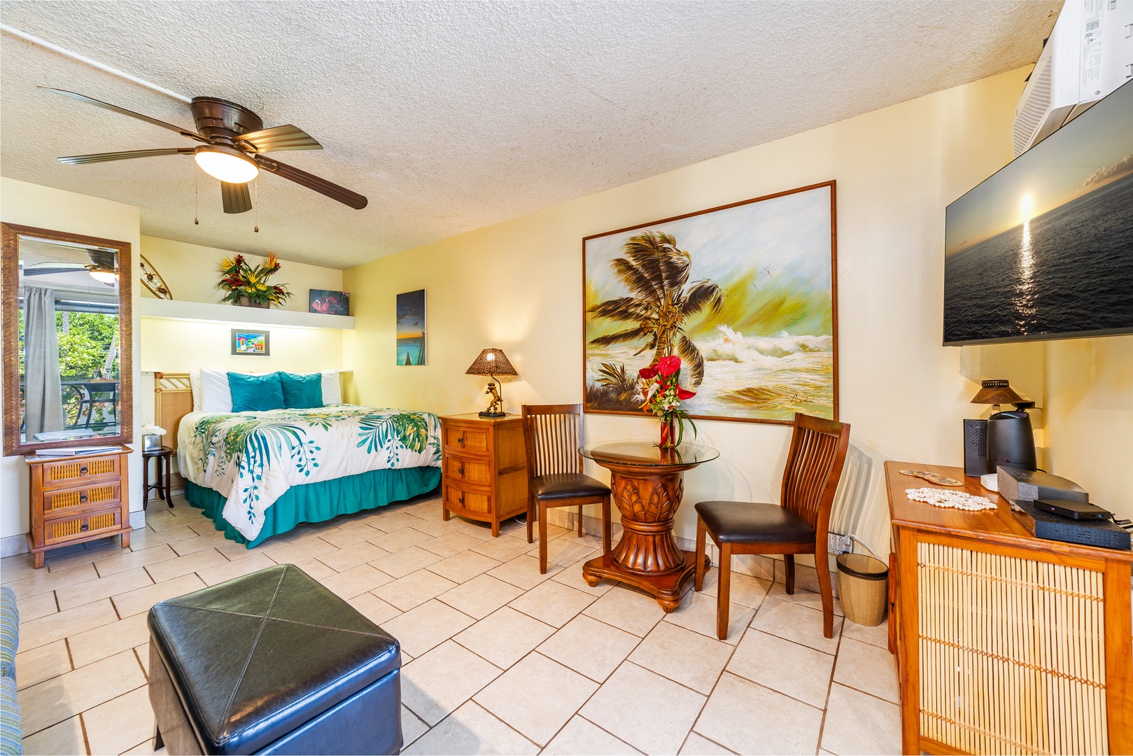 Your tropical retreat blends comfort and island charm, with a plush bed, breezy ceiling fan, coastal artwork, and a cozy sitting area for morning coffee.