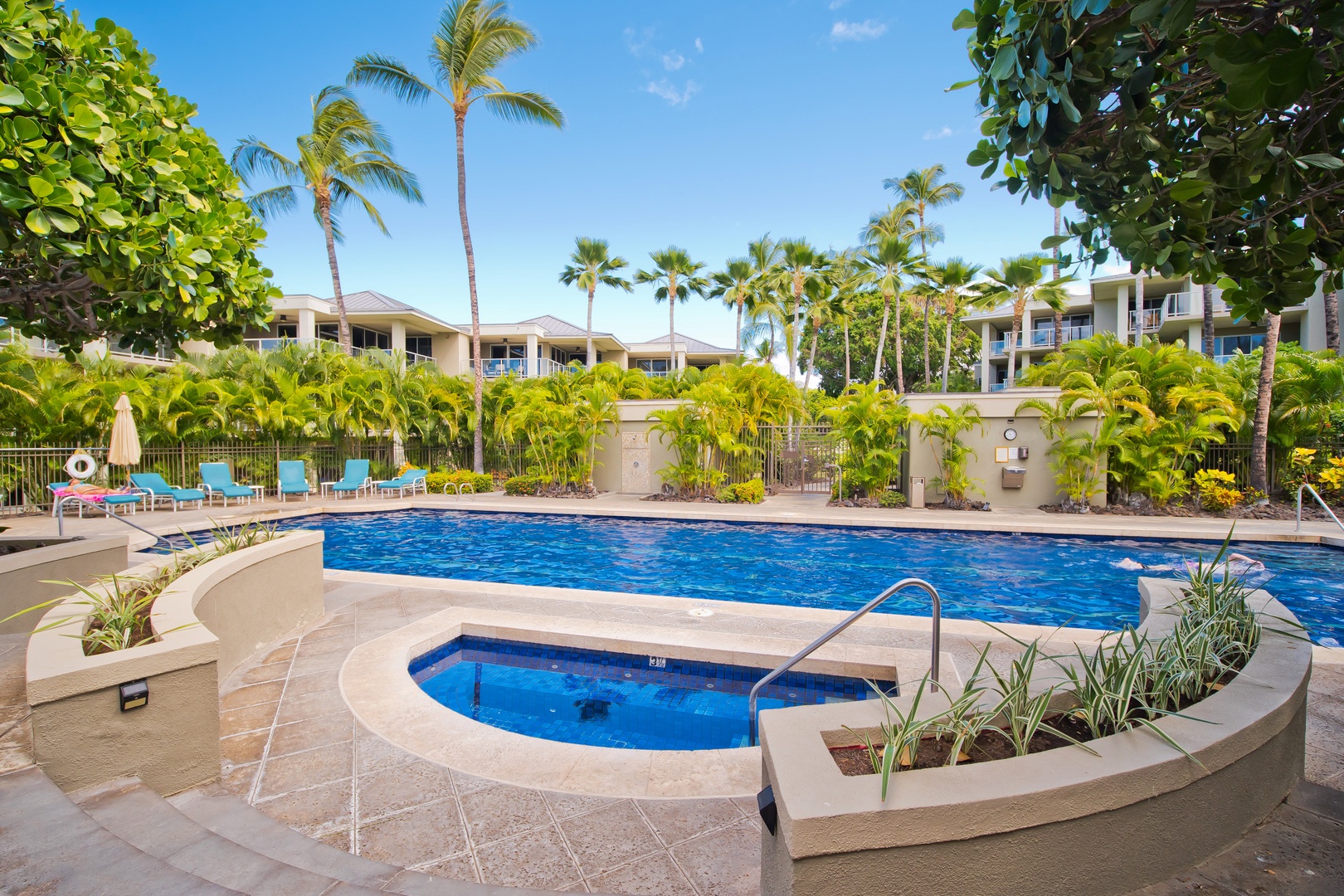 Tropical resort featuring a sparkling pool and hot tub surrounded by swaying palms, landscaped gardens, and lounge seating under sunny skies.