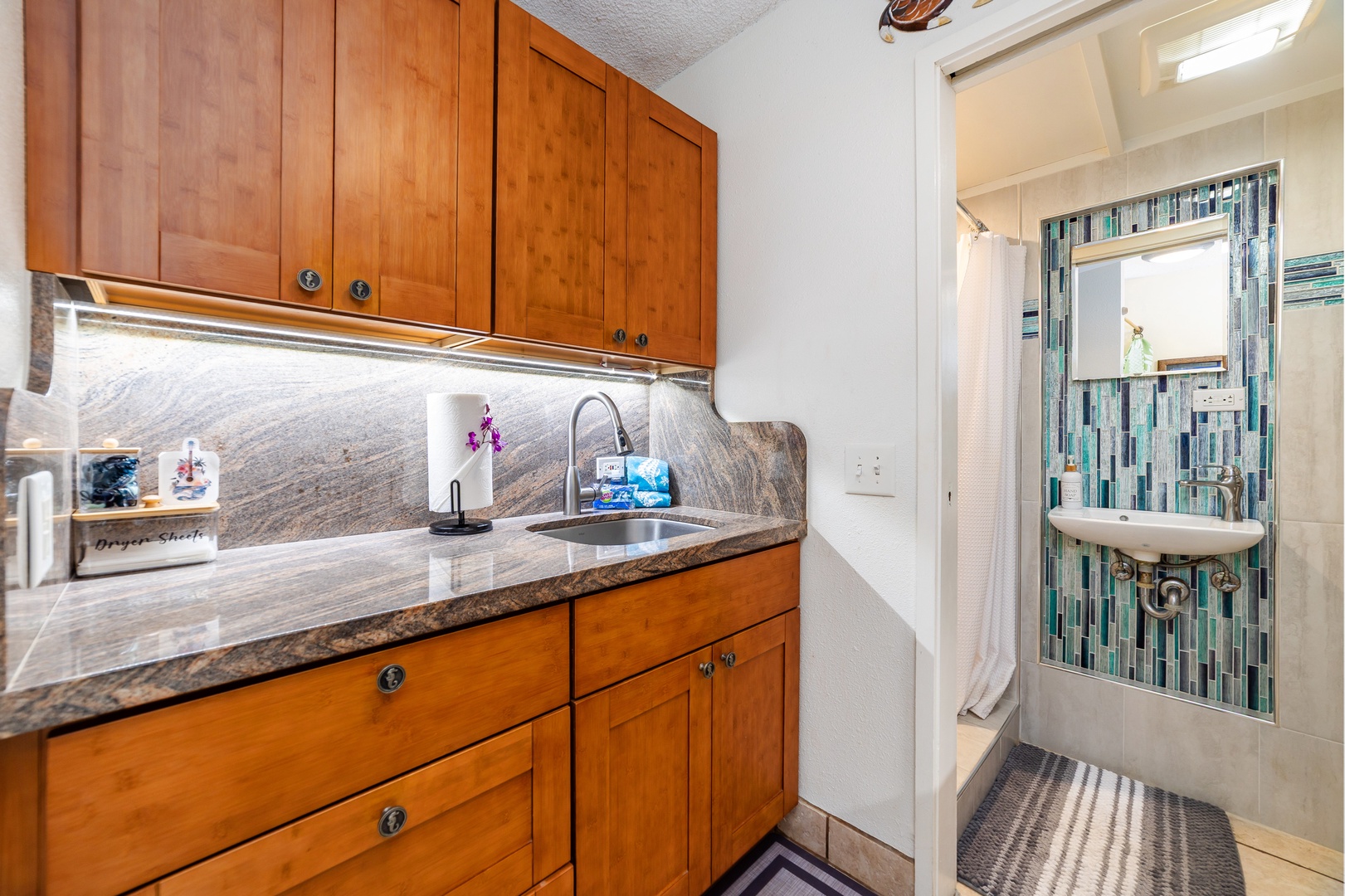 Your kitchenette features warm wood cabinetry, gleaming countertops, and under-cabinet lighting that makes meal prep a breeze. The adjacent bathroom offers modern tiled finishes for your refreshment.