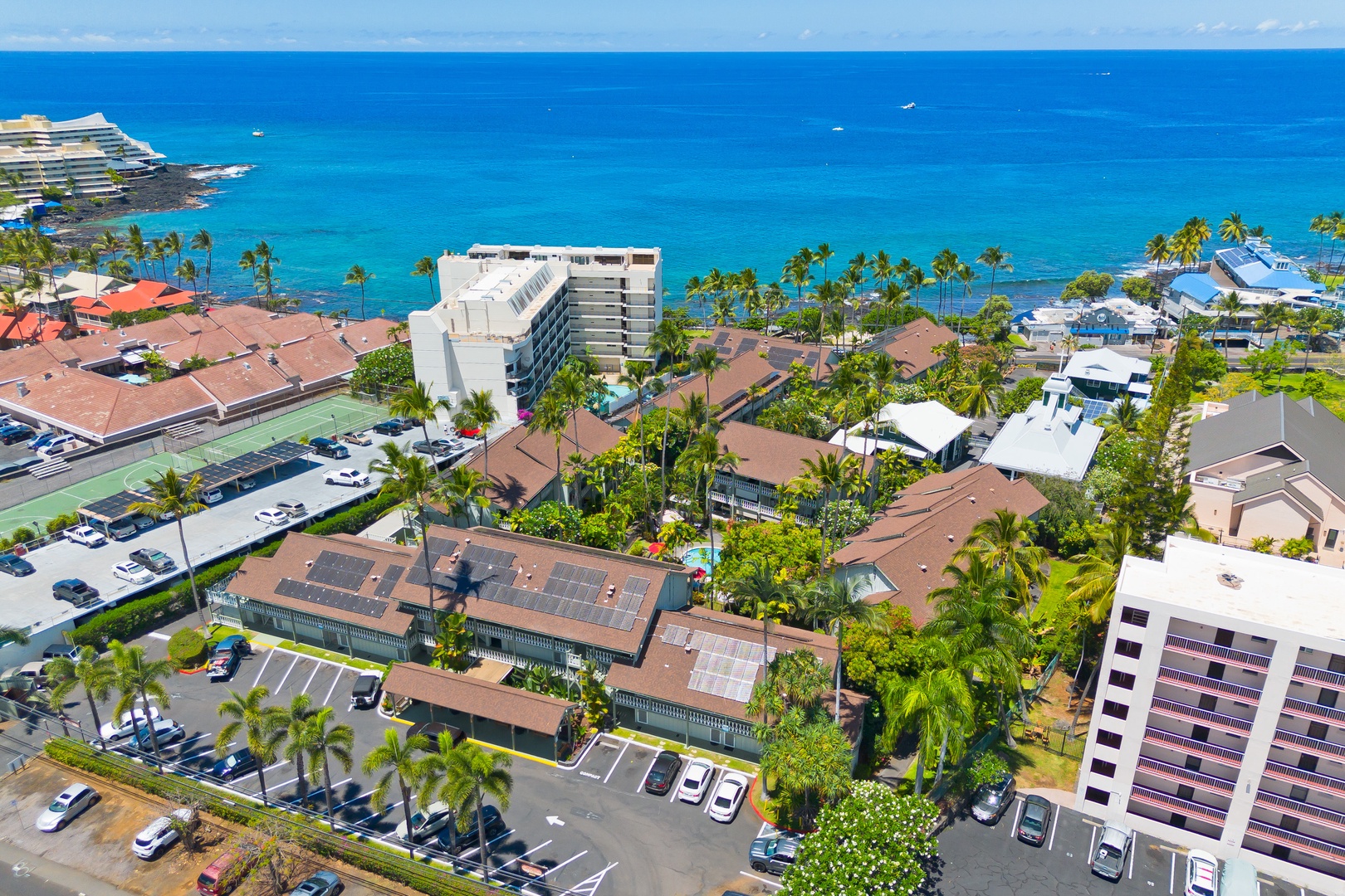 This oceanfront property sits steps from crystal-blue waters, surrounded by swaying palms and neighboring island-style buildings in a vibrant coastal community.