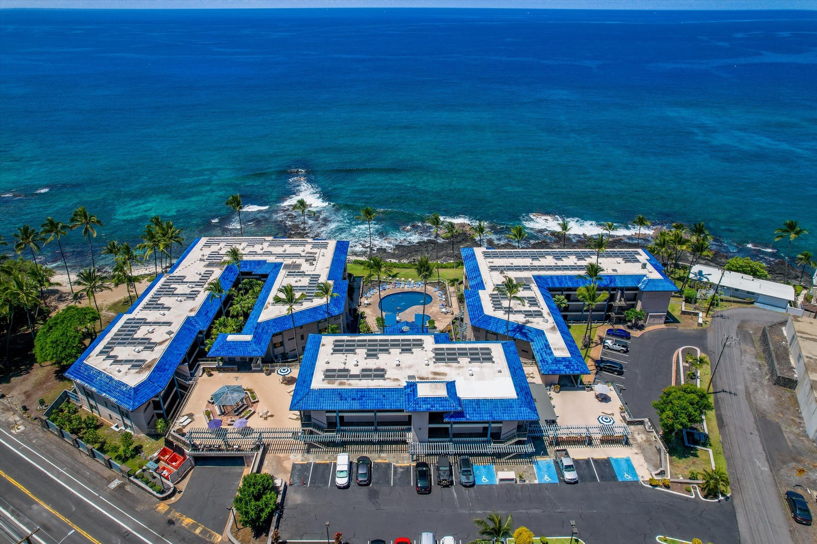 Kona Reef features a distinctive blue-roofed design, nestled along crystal-clear turquoise waters with palm trees.