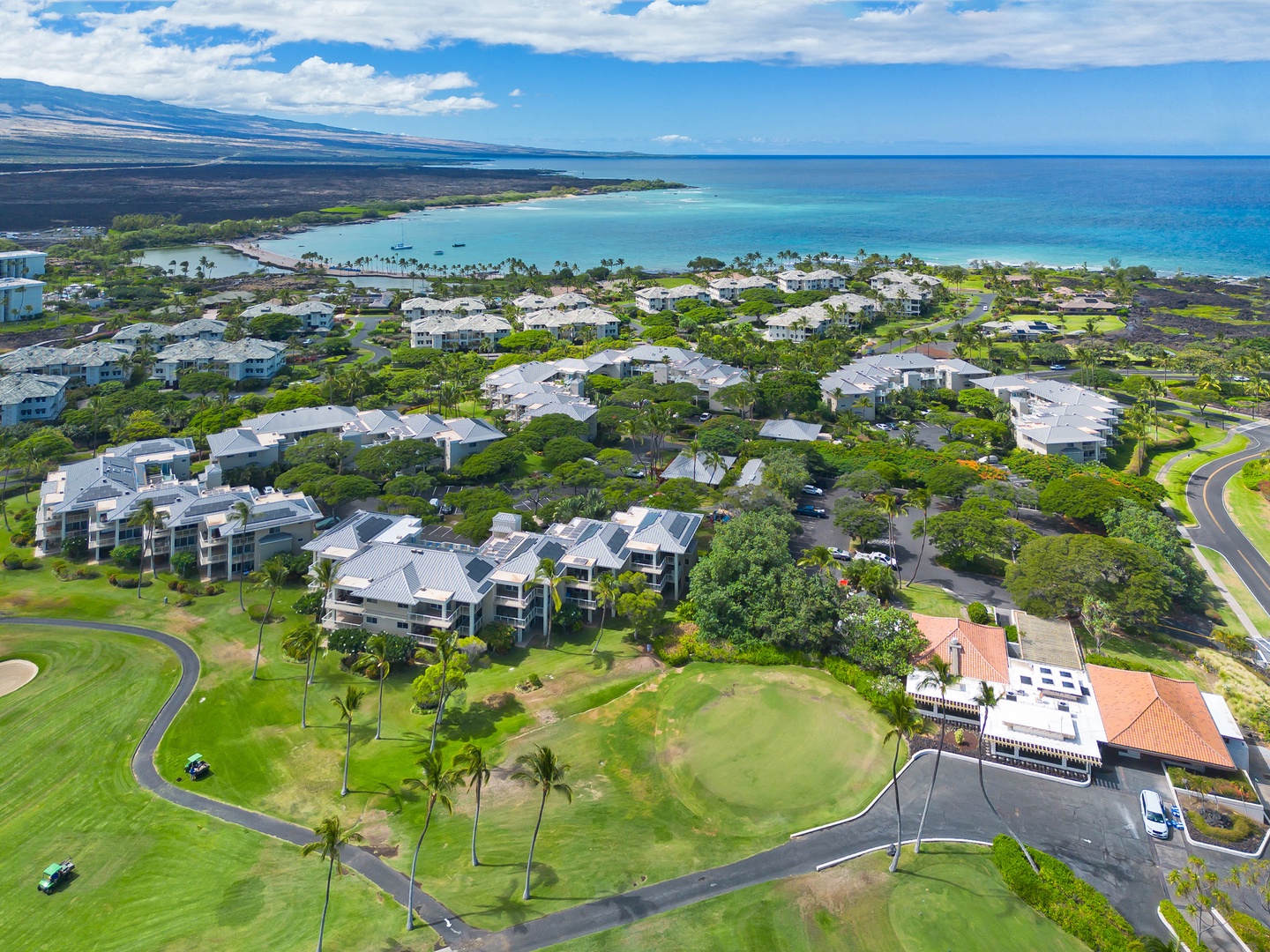 Aerial view of a beachfront resort community featuring low-rise residential buildings, manicured golf course fairways, tropical landscaping, and direct access to pristine turquoise waters and sandy beaches.