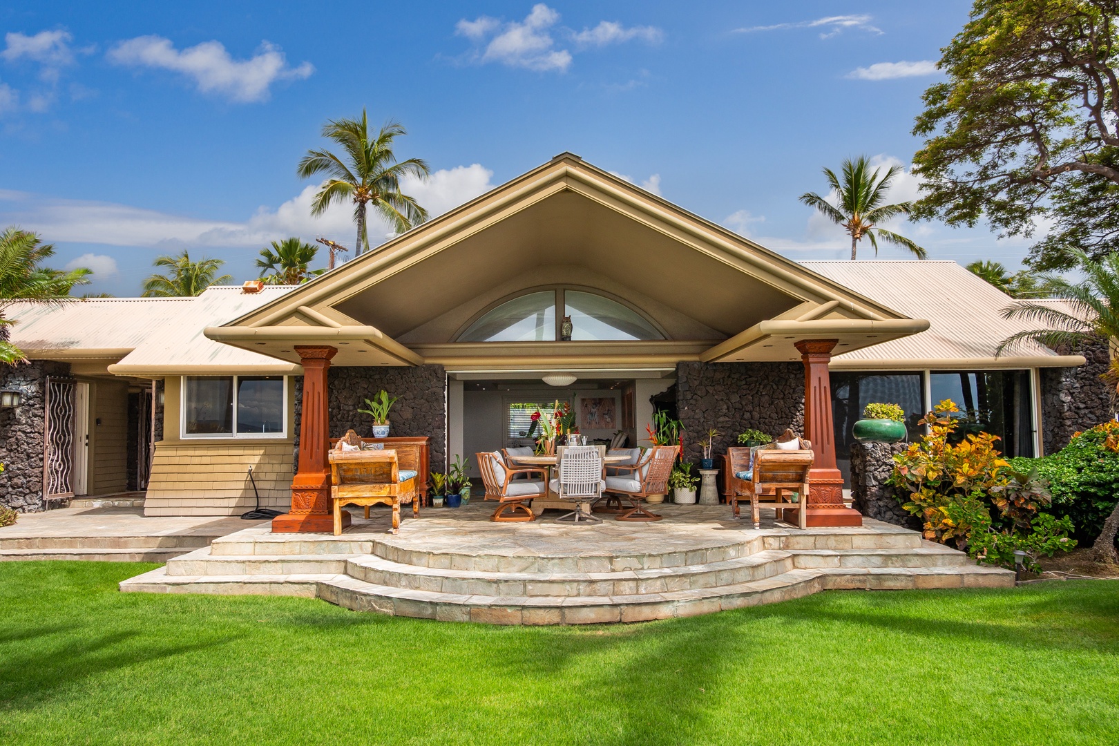 A tropical paradise framed by swaying palms and lush landscaping, this inviting property features a distinctive covered outdoor living area with elegant columns and carefully curated seating.