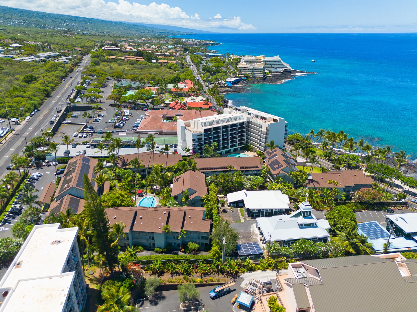Aerial view of the coastal property surrounded by lush tropical landscaping along the scenic Hawaiian shoreline, with nearby beaches and resort area.