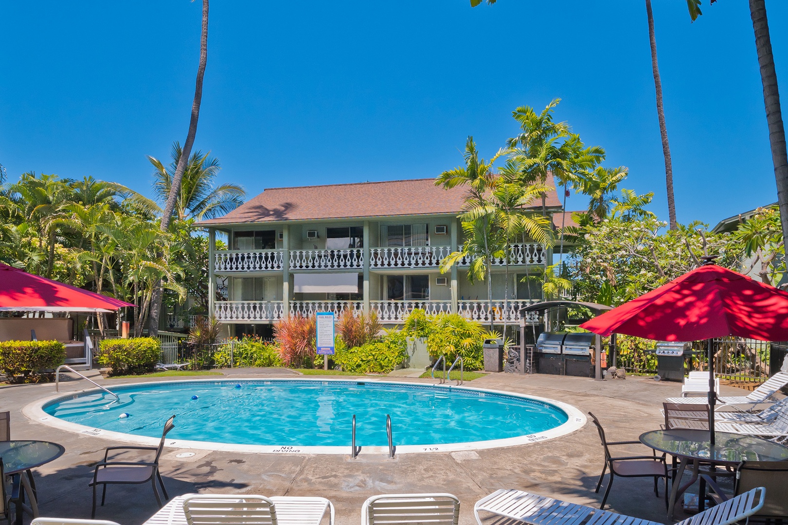 A sparkling pool sits beneath swaying palms, framed by the property's charming balconies and lush tropical gardens—your perfect spot to soak up sunny Hawaiian days.