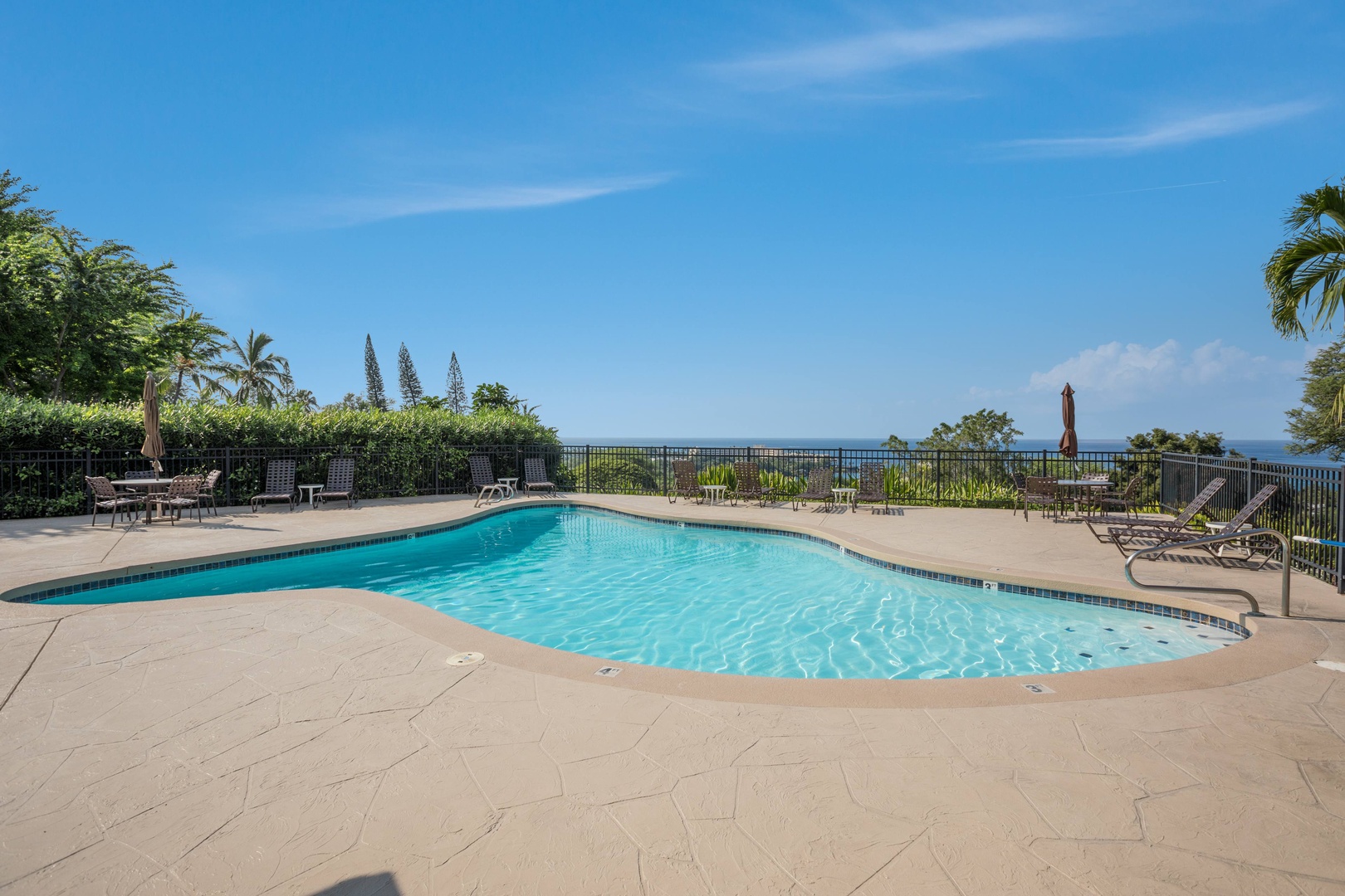 The pool deck offers a peaceful oceanfront setting framed by swaying palms, lush hedges, and distant coastal views. A tranquil spot to unwind outdoors within the resort grounds.