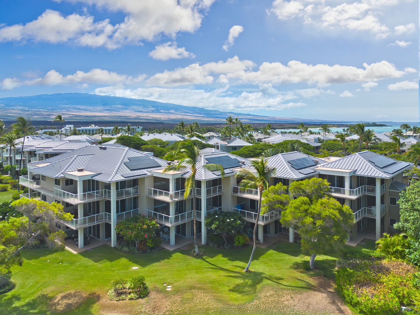Aerial view showcasing the modern tropical resort buildings set among lush landscaping, with mountain and ocean scenery visible in the surrounding area.
