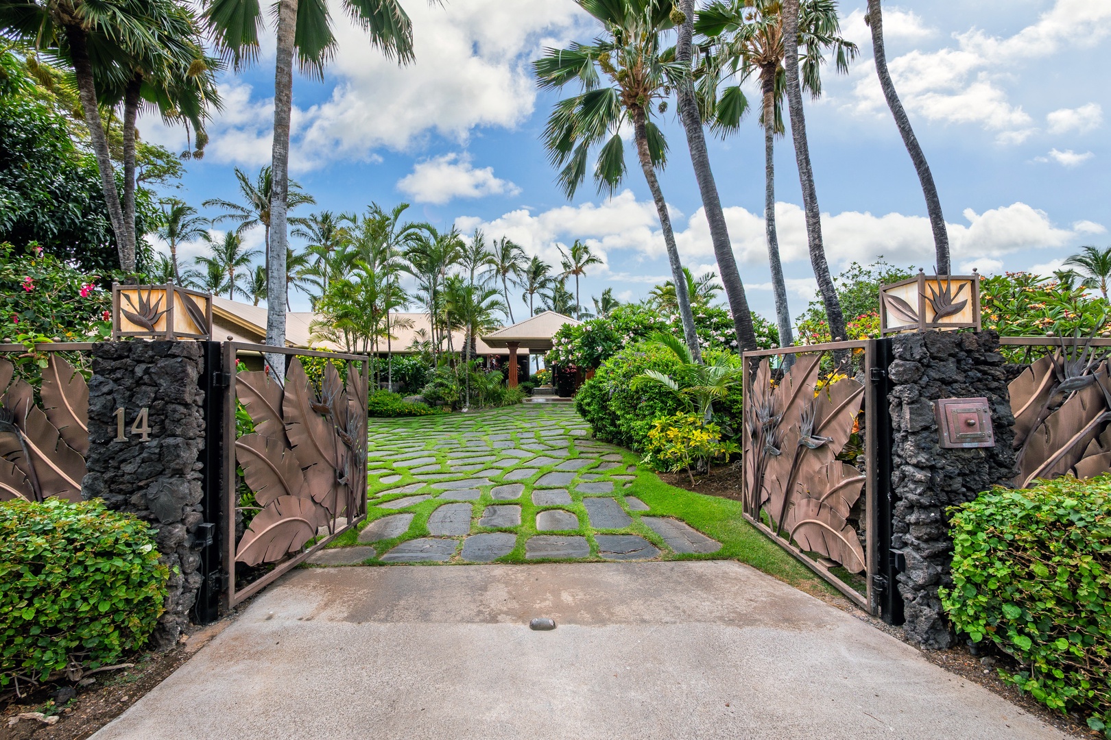 Private Gated Entry - A tropical entrance framed by custom gates and lush palms leads through manicured gardens to the property's private retreat, offering an inviting arrival experience.