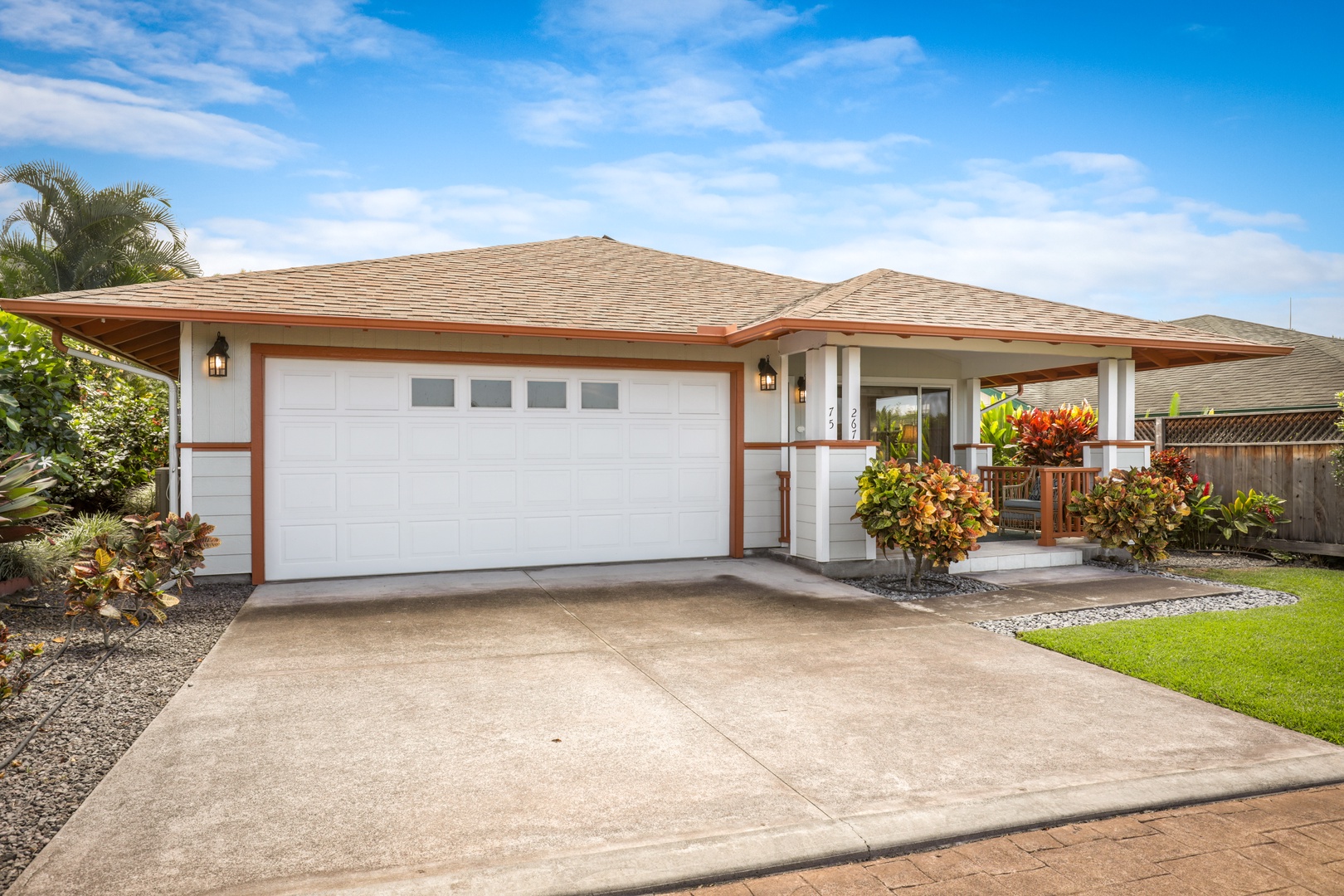 A welcoming single-story home features tropical landscaping, a spacious two-car garage, and covered entryway framed by vibrant greenery under open skies—your island retreat awaits.