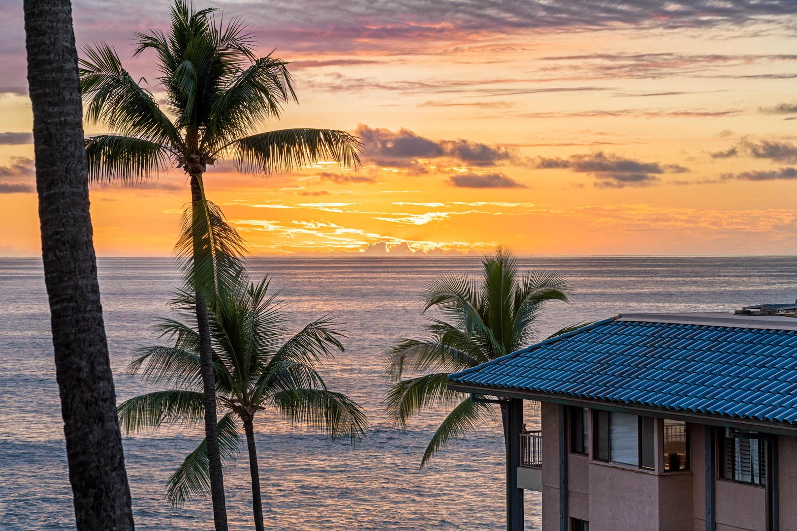 A stunning beachfront property with iconic palm trees and brilliant sunset colors painting the sky over the calm ocean waters.