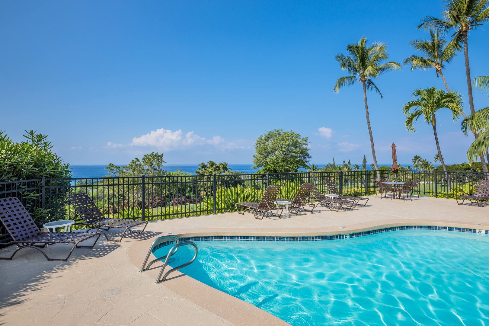 A sparkling pool deck overlooking lush tropical gardens and brilliant ocean views, framed by swaying palms and loungers ready for your island escape.