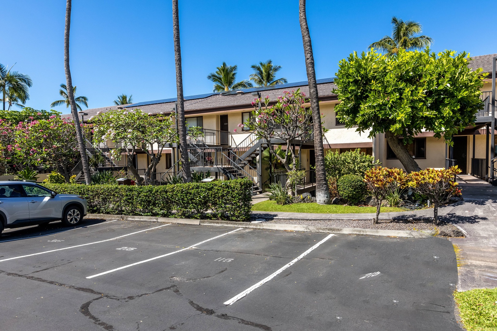 Two-story tropical property with lush landscaping, towering palms, and convenient parking in a sunny Hawaiian setting.