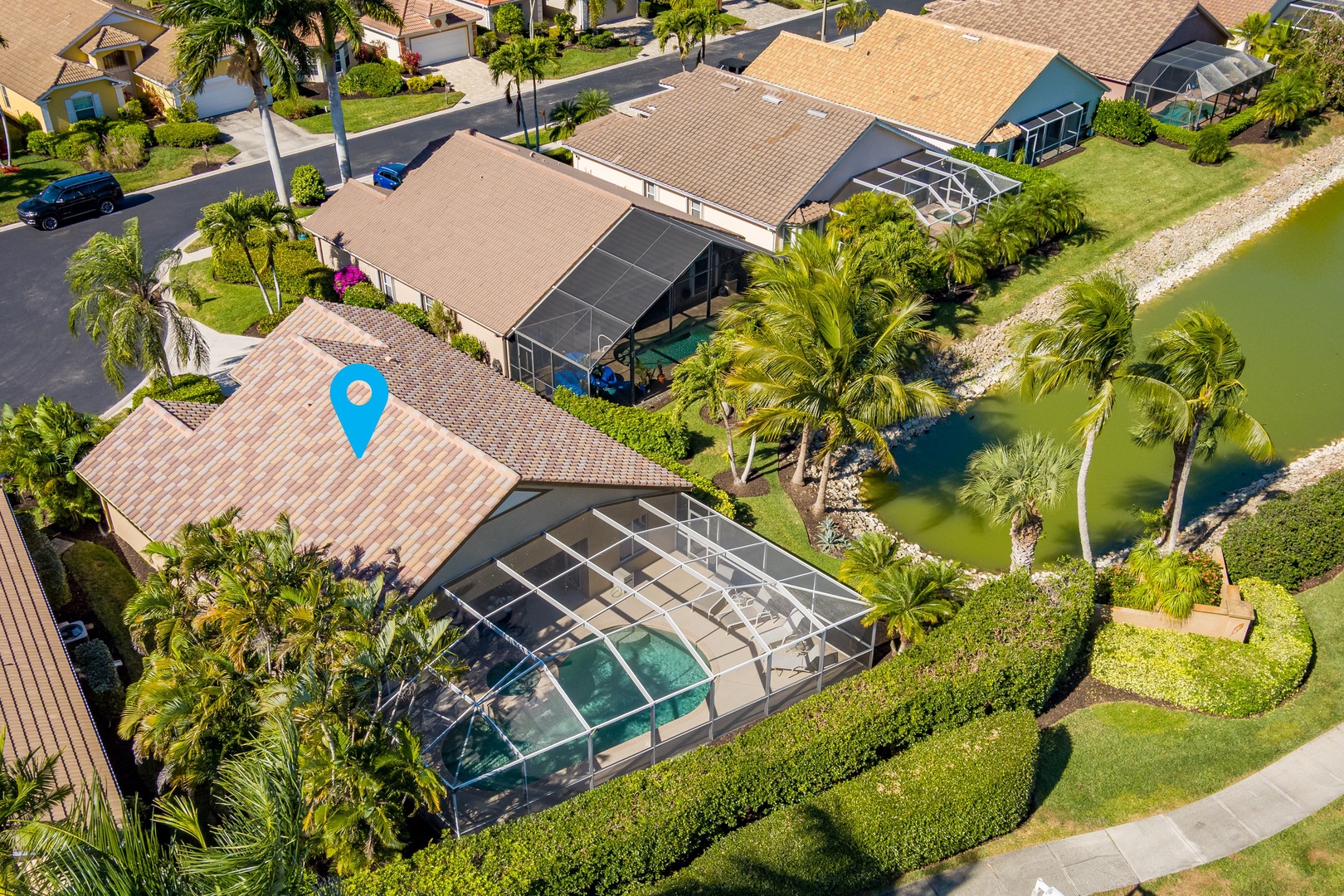 Aerial view of waterfront vacation home featuring screened pool, tropical landscaping, and canal access in peaceful residential community.