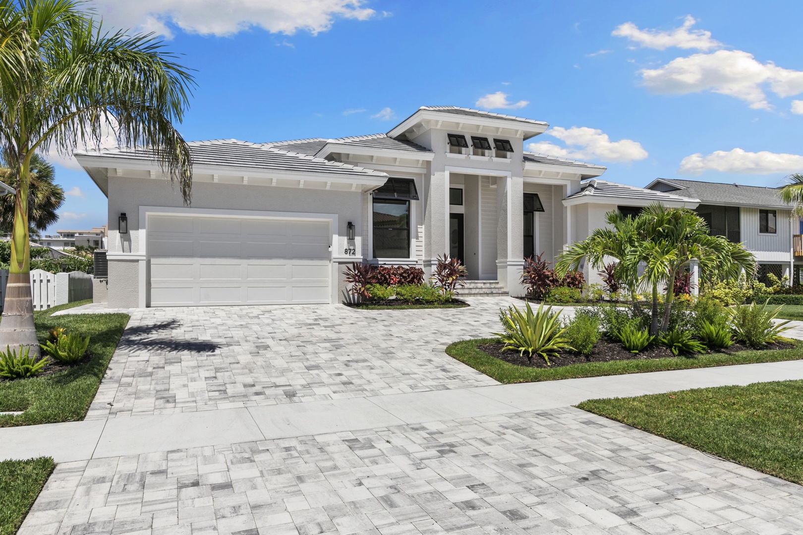 This modern vacation home showcases sleek architectural lines and lush tropical landscaping, creating an inviting arrival experience in a quiet residential setting.