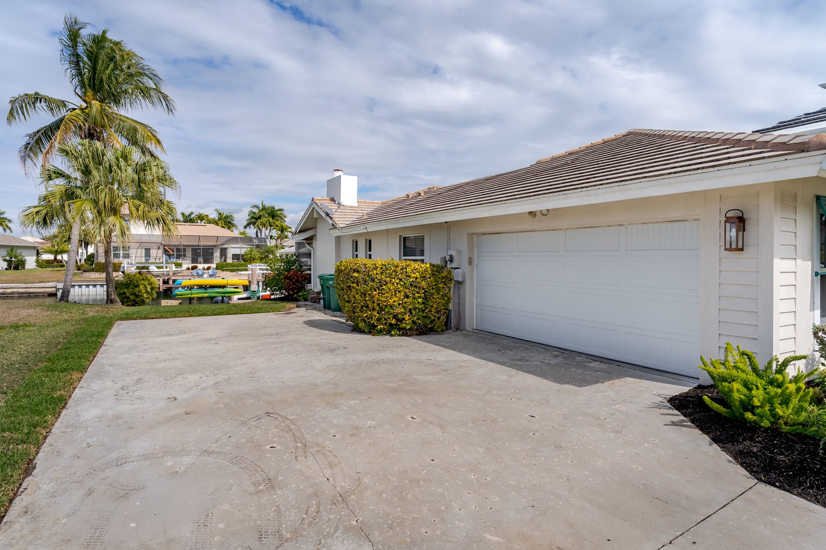 Single-story home with attached garage in tropical neighborhood setting with palm trees and manicured landscaping.