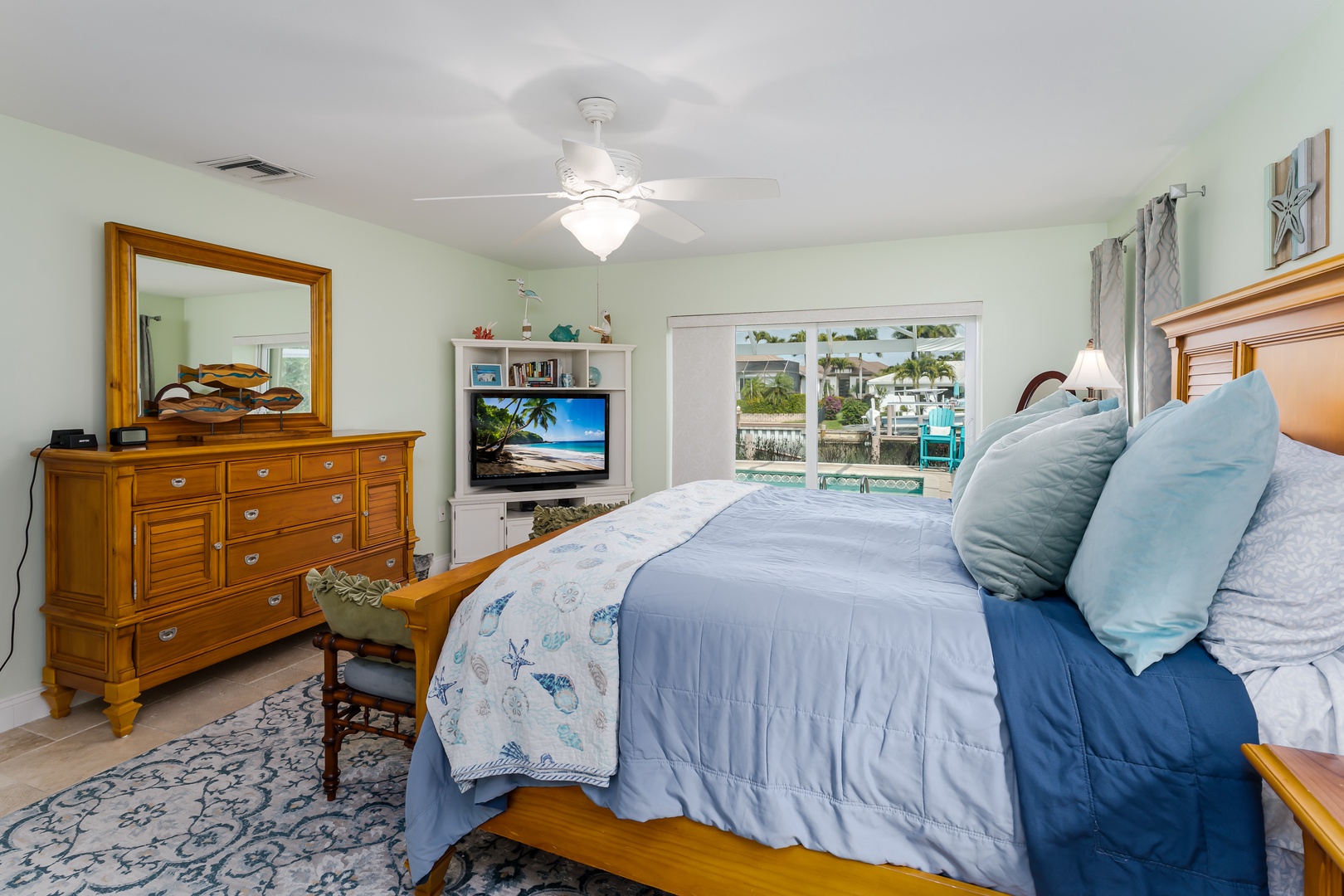 Your serene bedroom features coastal-inspired blue linens and warm wood furnishings, with waterfront views through bright windows.