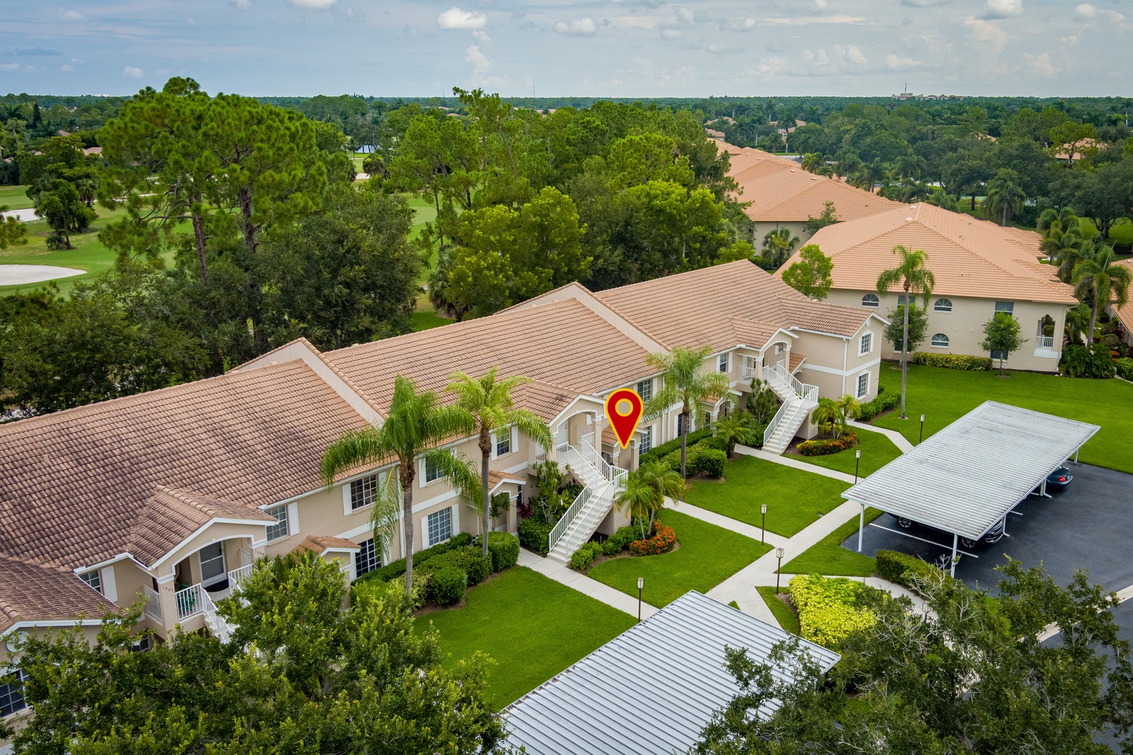 Aerial view of the rental property showcasing spacious landscaped grounds, tropical palm trees, covered parking, and the surrounding lush residential neighborhood.