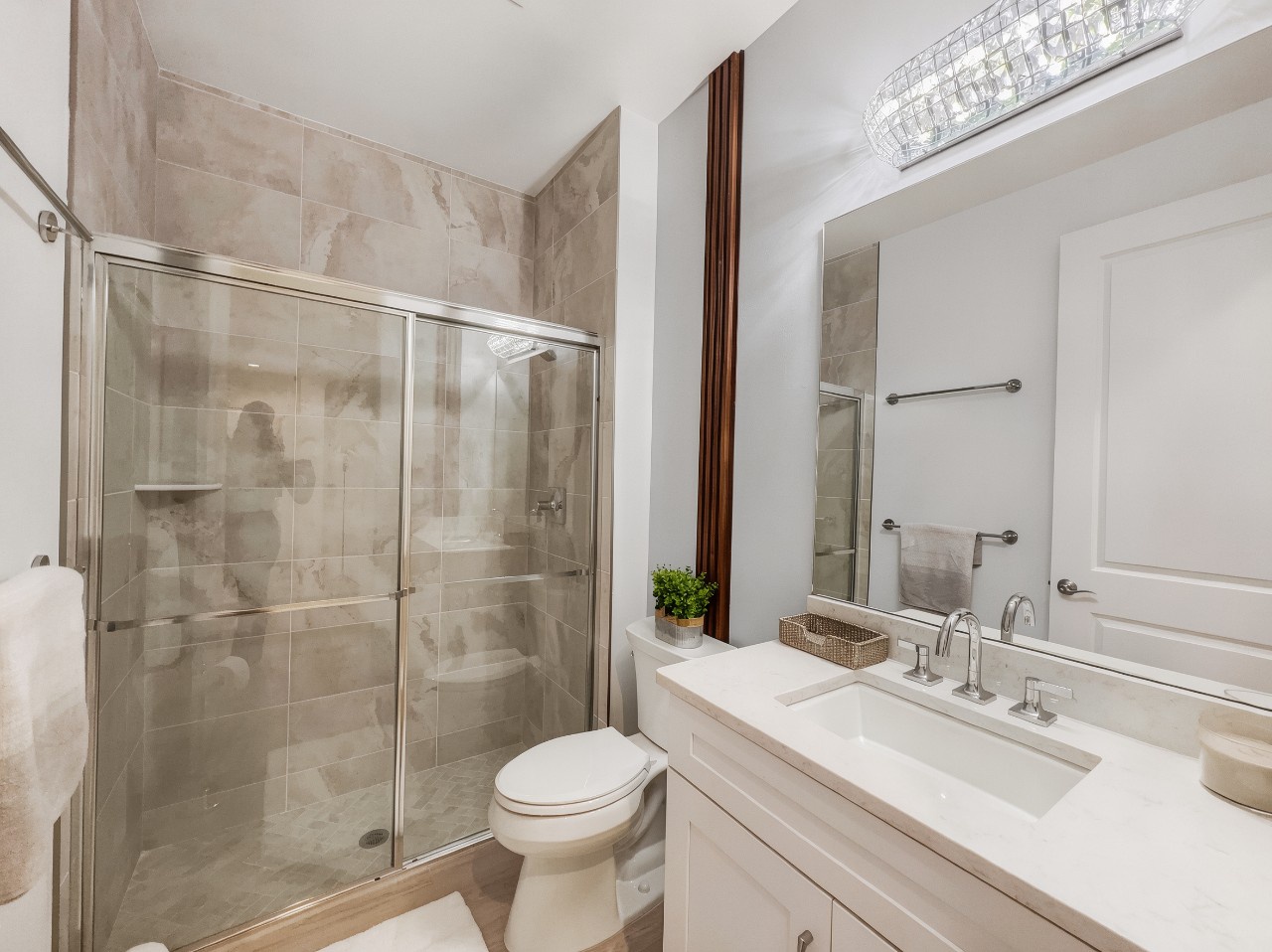 Your private bathroom feels serene and spa-like, with elegant marble-style tiles, a spacious glass-enclosed shower, and a pristine vanity ready for your morning routine.