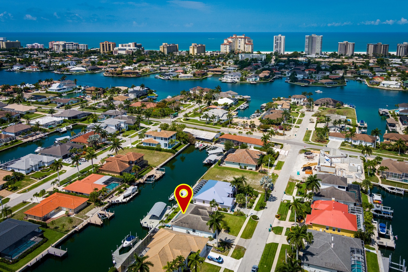 An aerial view of a waterfront neighborhood with canal-access homes, private docks, and nearby beach towers visible in the distance.