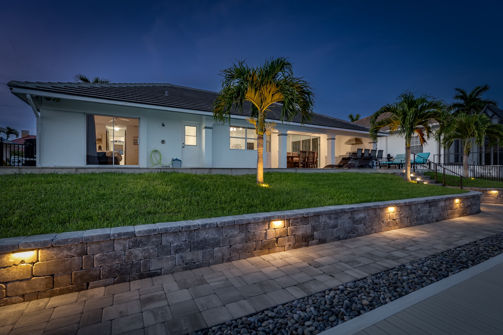 A modern vacation retreat showcasing elegant architecture and tropical landscaping with accent lighting highlighting the property's welcoming entrance at dusk.
