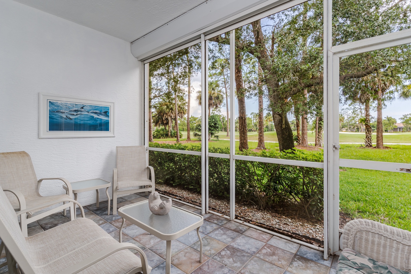 Unwind on your private screened patio, where comfortable seating invites you to soak in peaceful garden views beneath towering palms and mature oak trees.