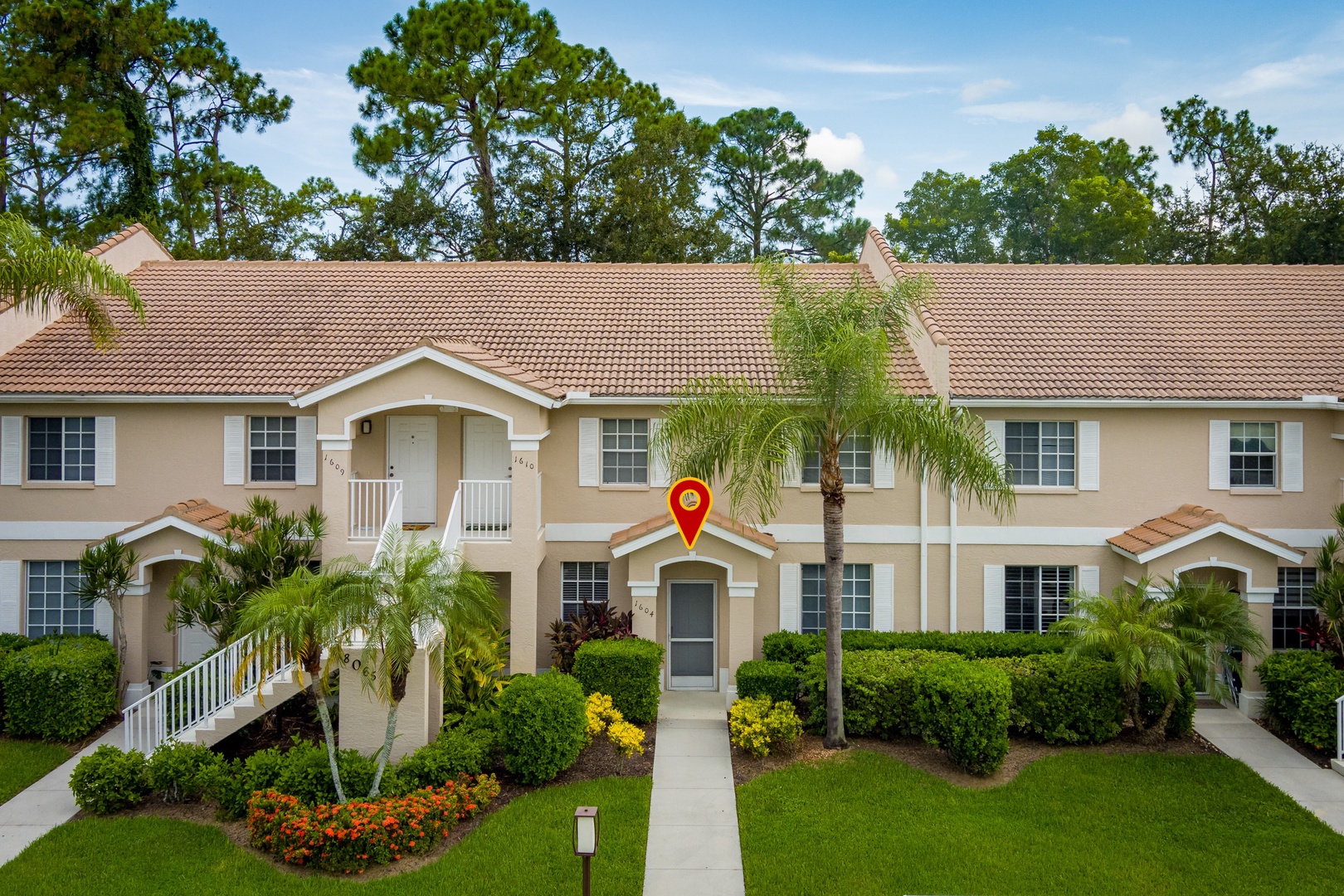 A multi-unit vacation property situated in a lush tropical setting, surrounded by mature palms and pine trees. The location marker identifies this specific unit within the well-maintained complex.