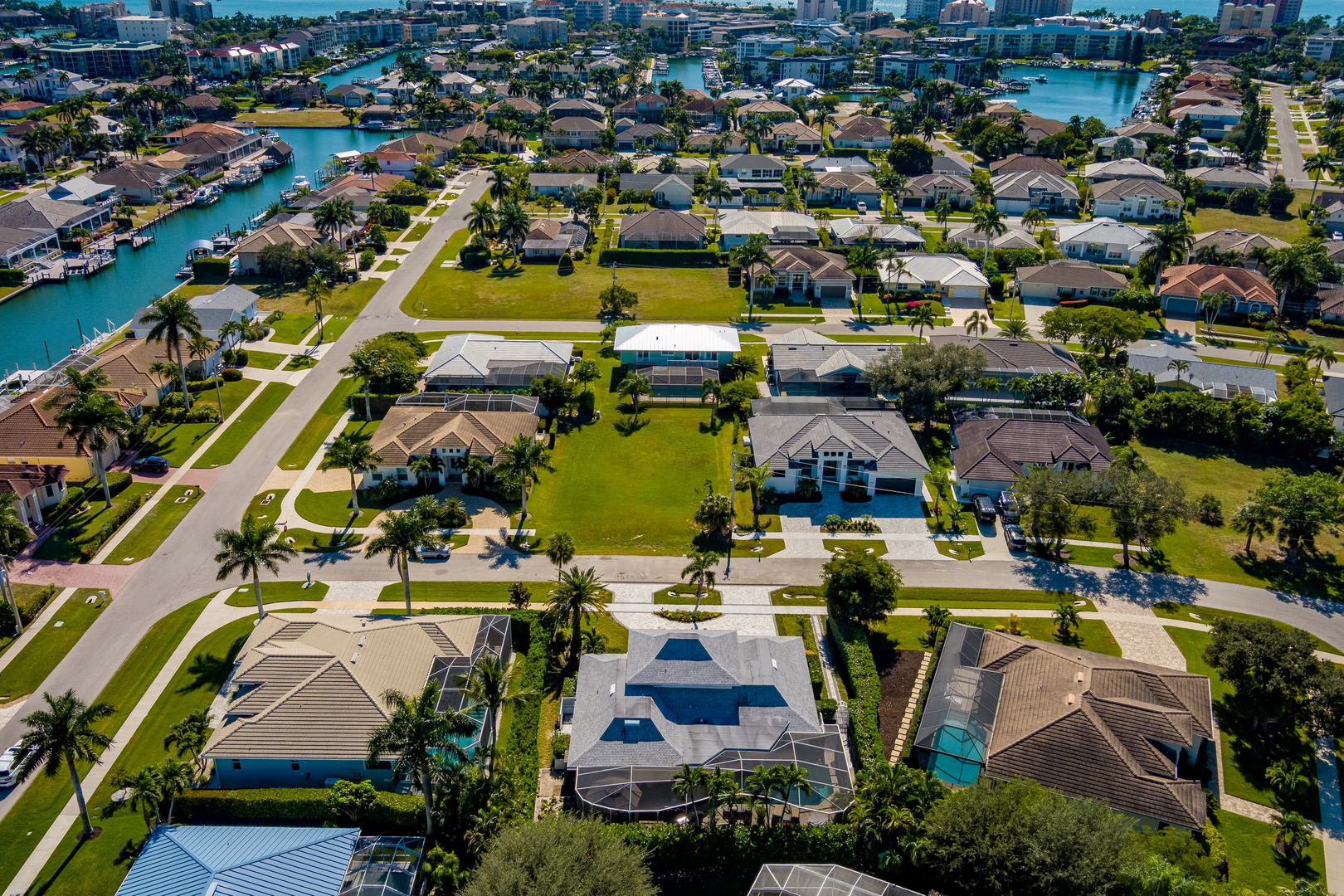 Aerial view of a waterfront neighborhood featuring single-family homes with pools, landscaped yards, and canal access in a tropical setting.
