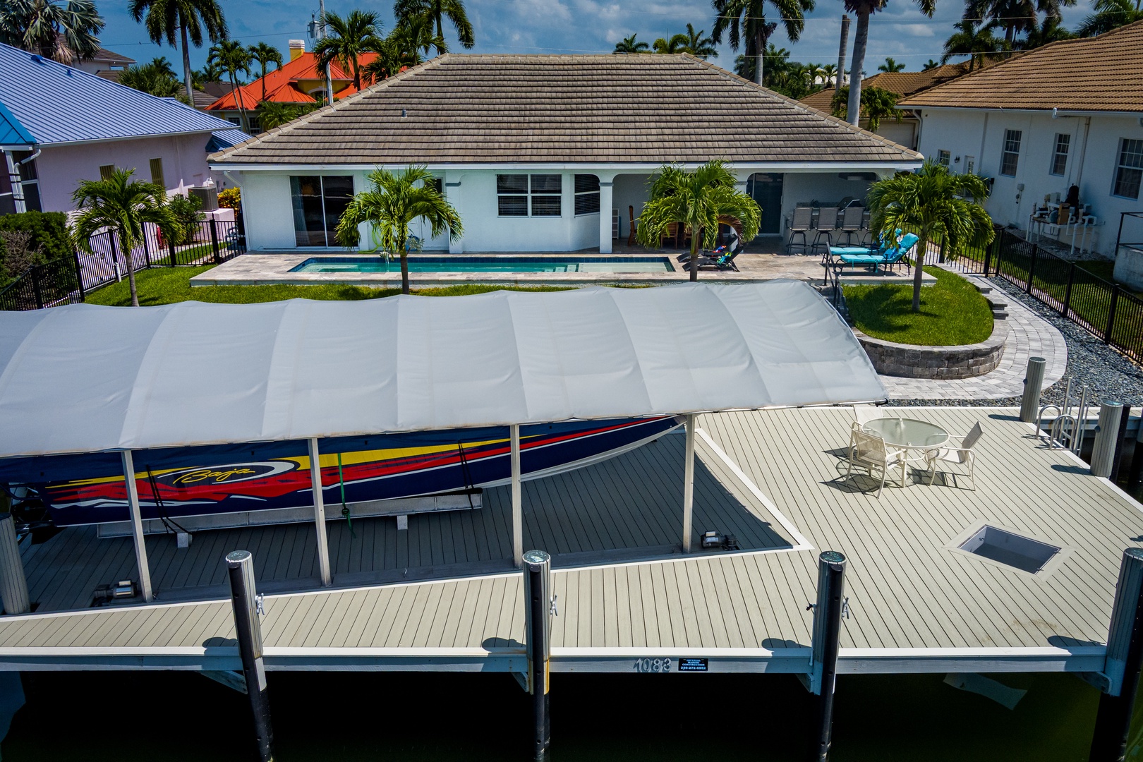Aerial view of a waterfront vacation home with private pool, boat dock, and lush tropical landscaping in a palm-lined neighborhood, perfect for a sunny Florida getaway.