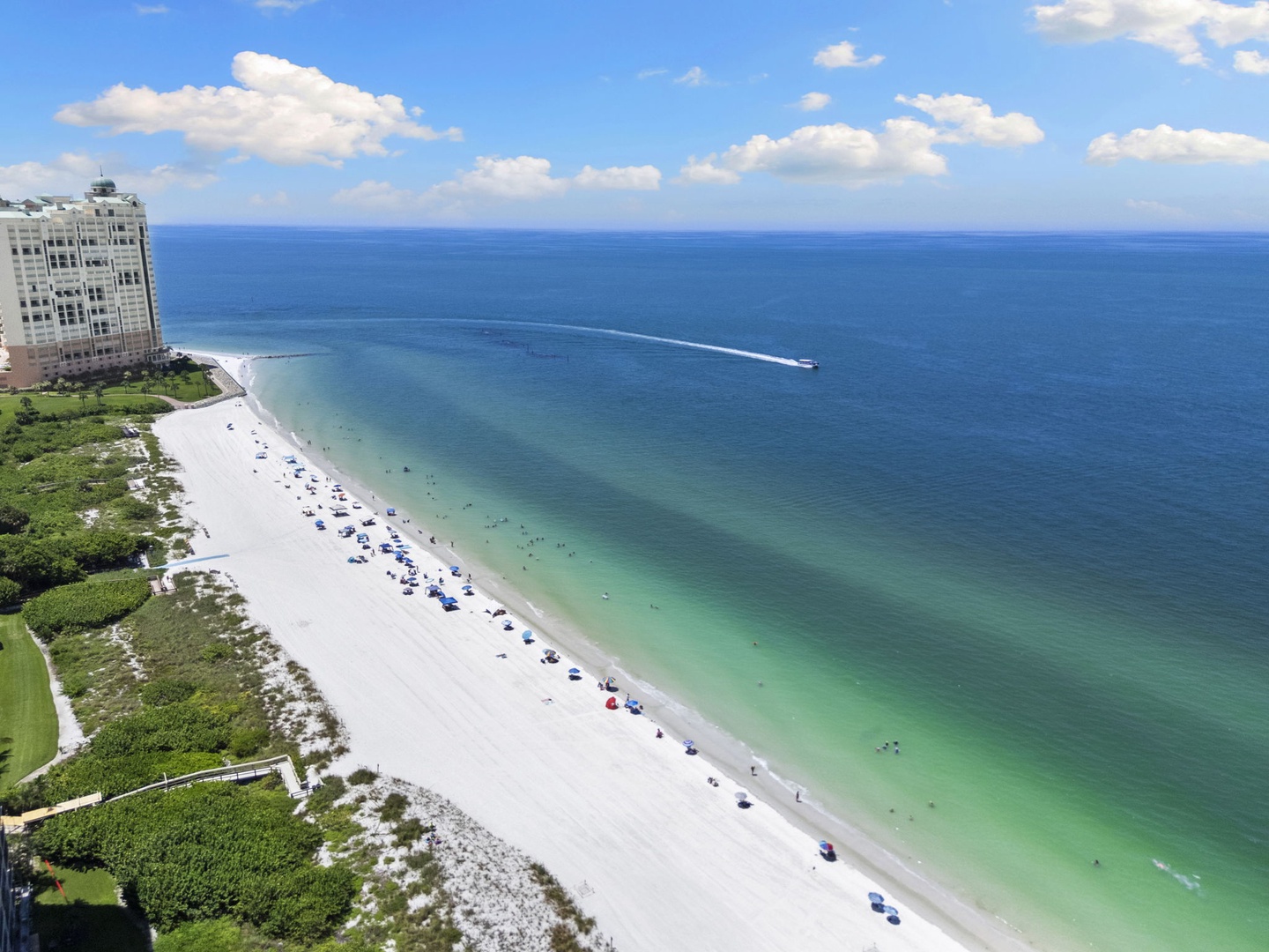 Aerial view of a pristine white sand beach with turquoise waters, beachfront property, and vibrant blue sky—a stunning coastal setting for a relaxing getaway.