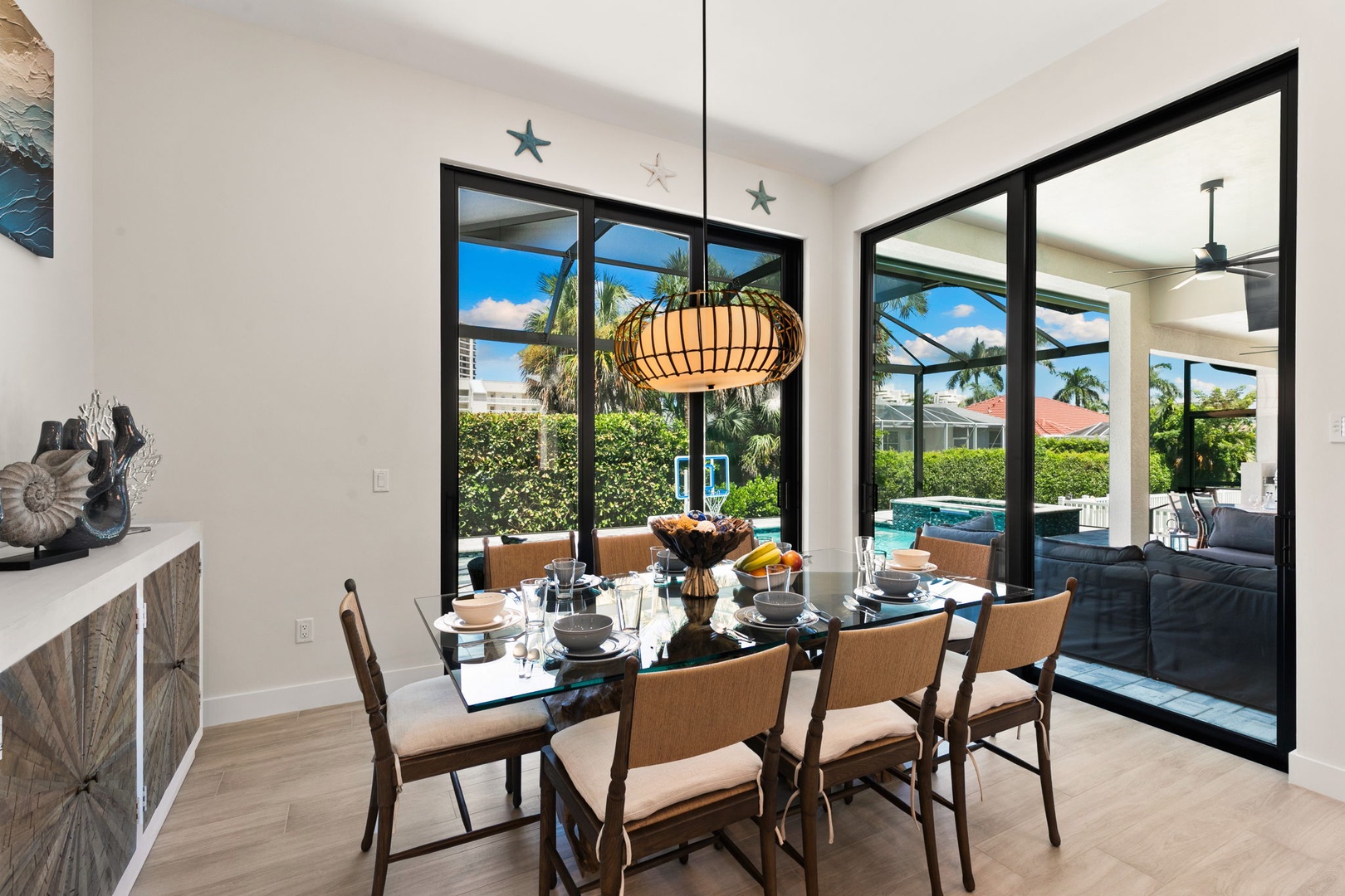 Gather around a stylish dining table where natural light floods through expansive glass doors, framing your private pool and lush tropical surroundings beyond.