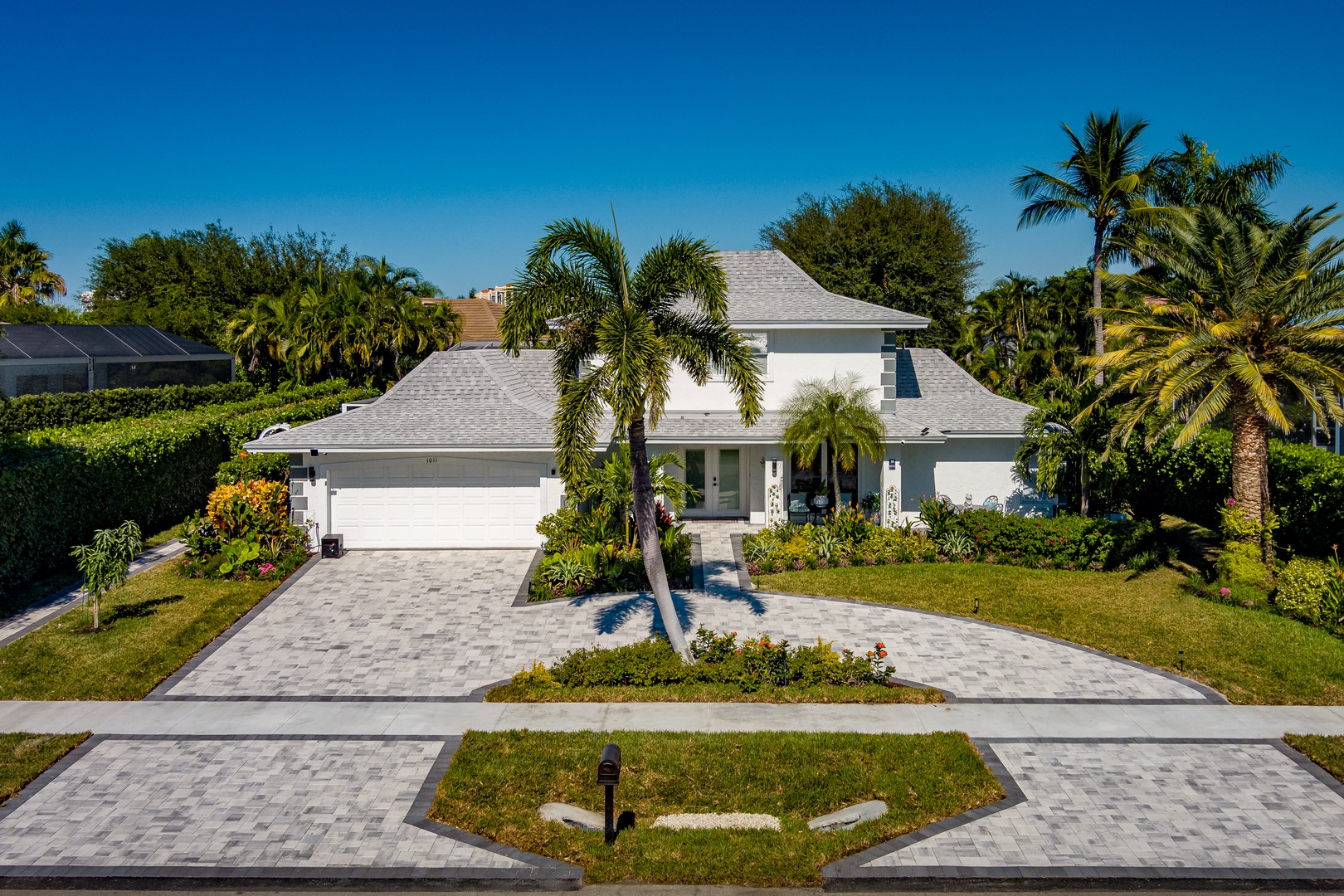 Modern white vacation home surrounded by tropical palms and lush landscaping in a sunny Florida neighborhood.