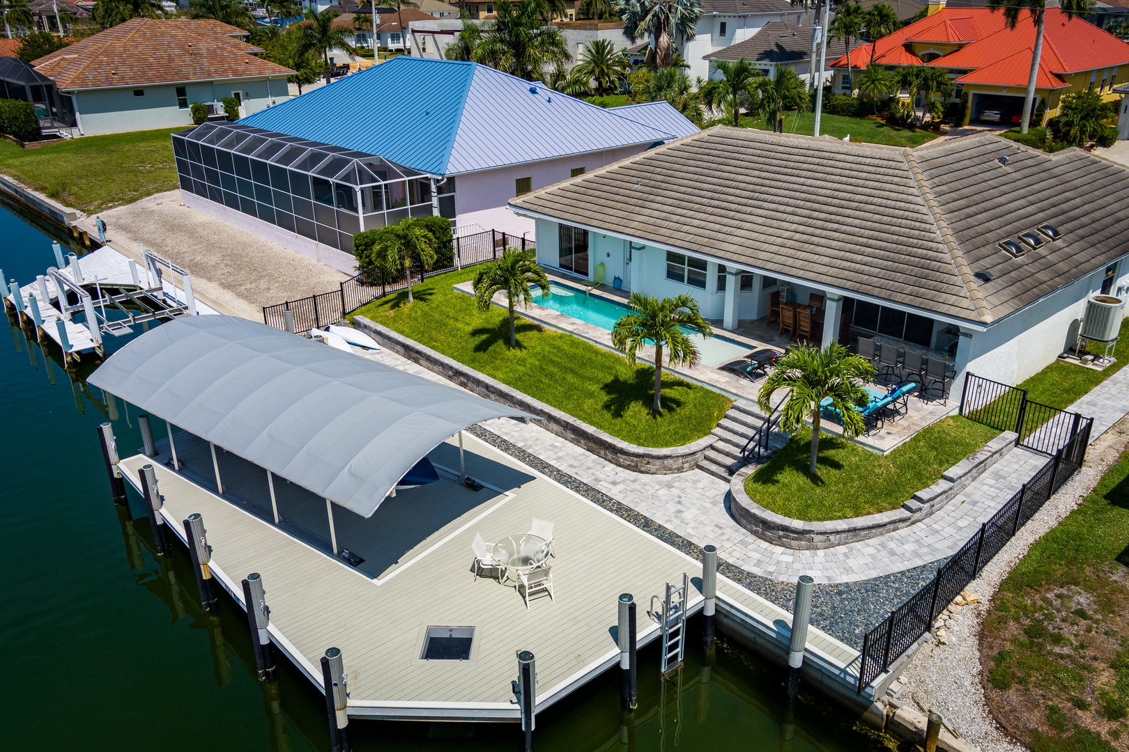 Aerial view of a waterfront vacation home featuring a private pool, spacious dock with covered boat lift, and lush tropical landscaping in a peaceful residential neighborhood.